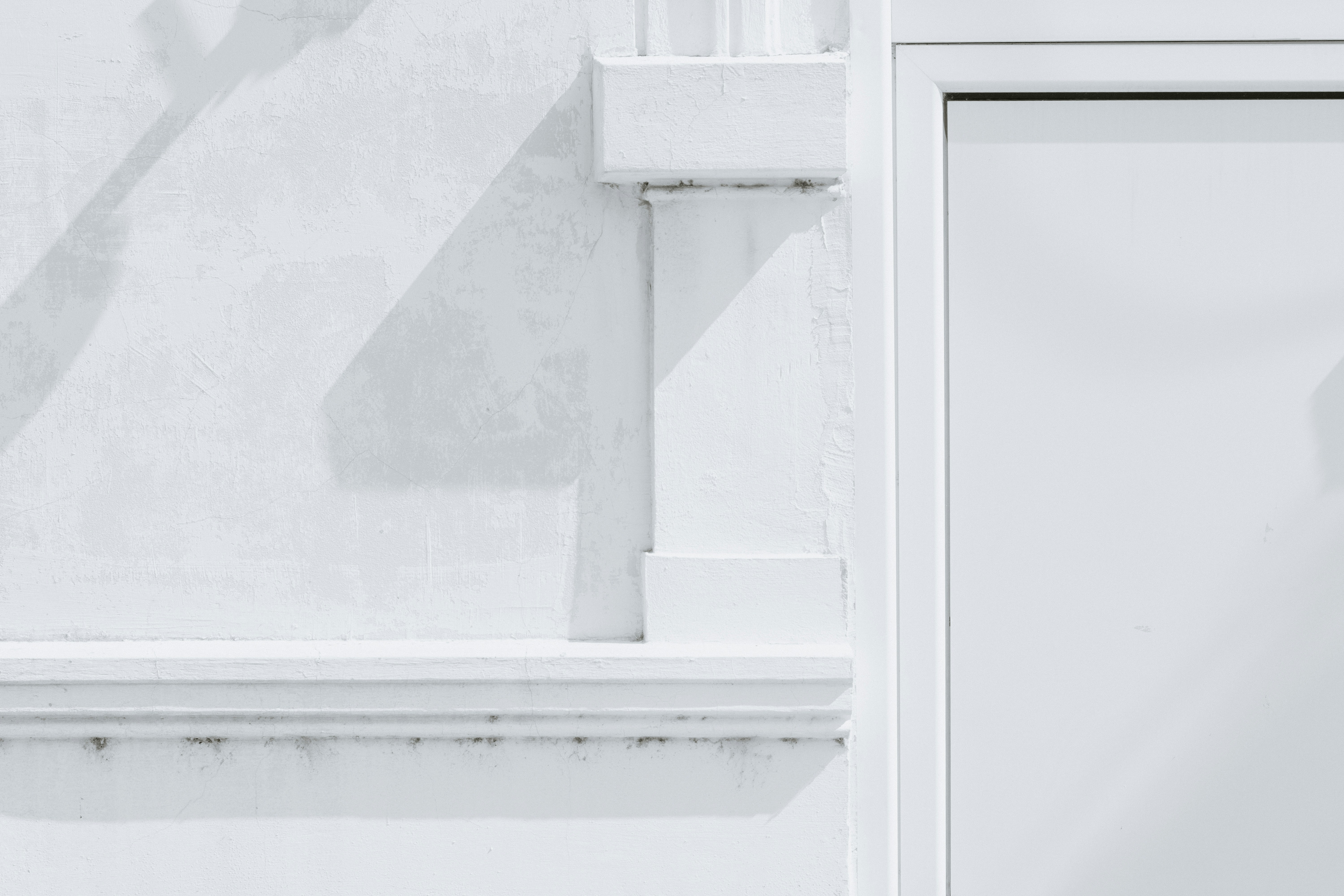 A white wall with architectural molding and a door frame in bright light