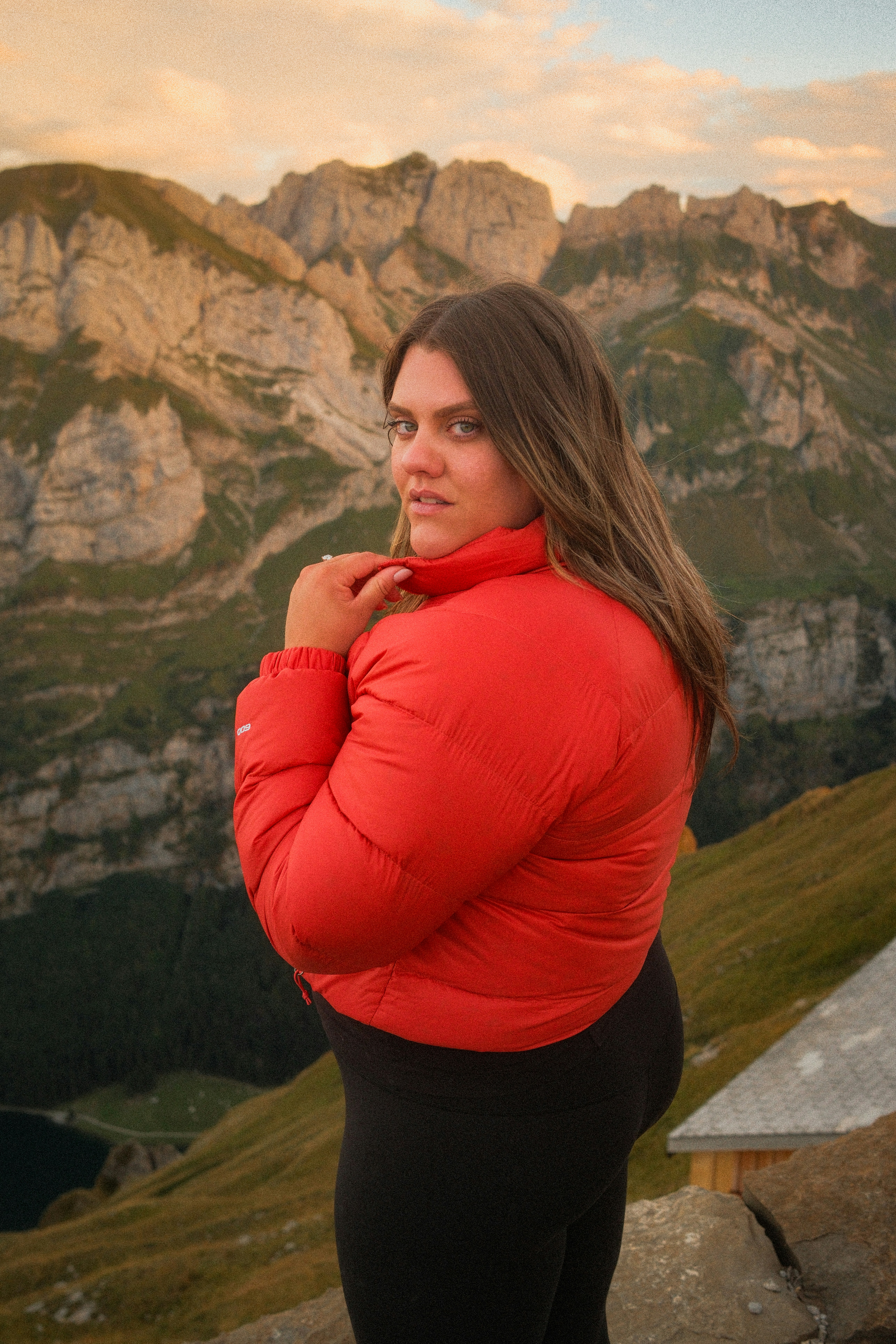 Une femme en doudoune rouge regardant en arrière les sommets des montagnes suisses