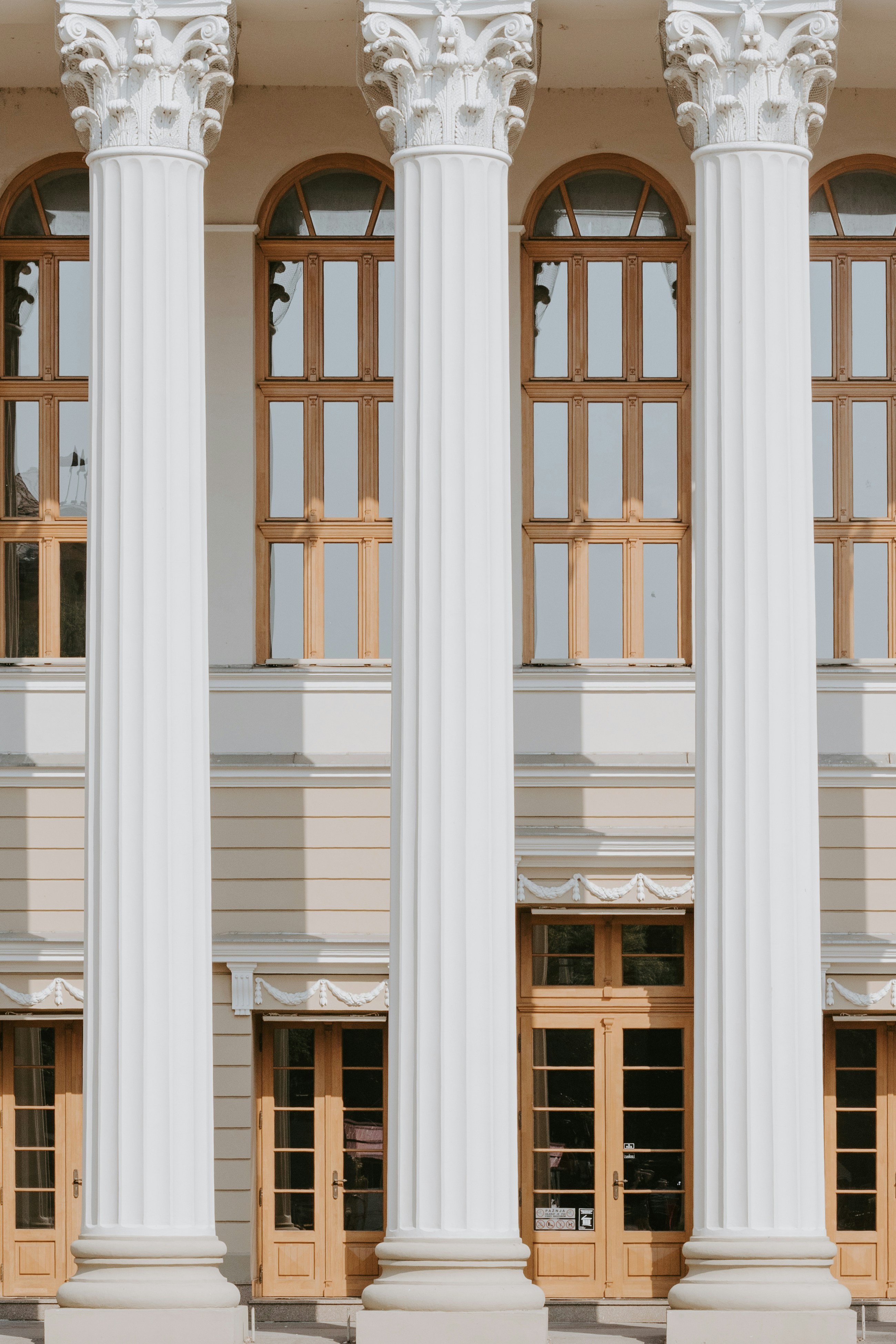 Three white fluted columns in front of a building with wooden framed windows