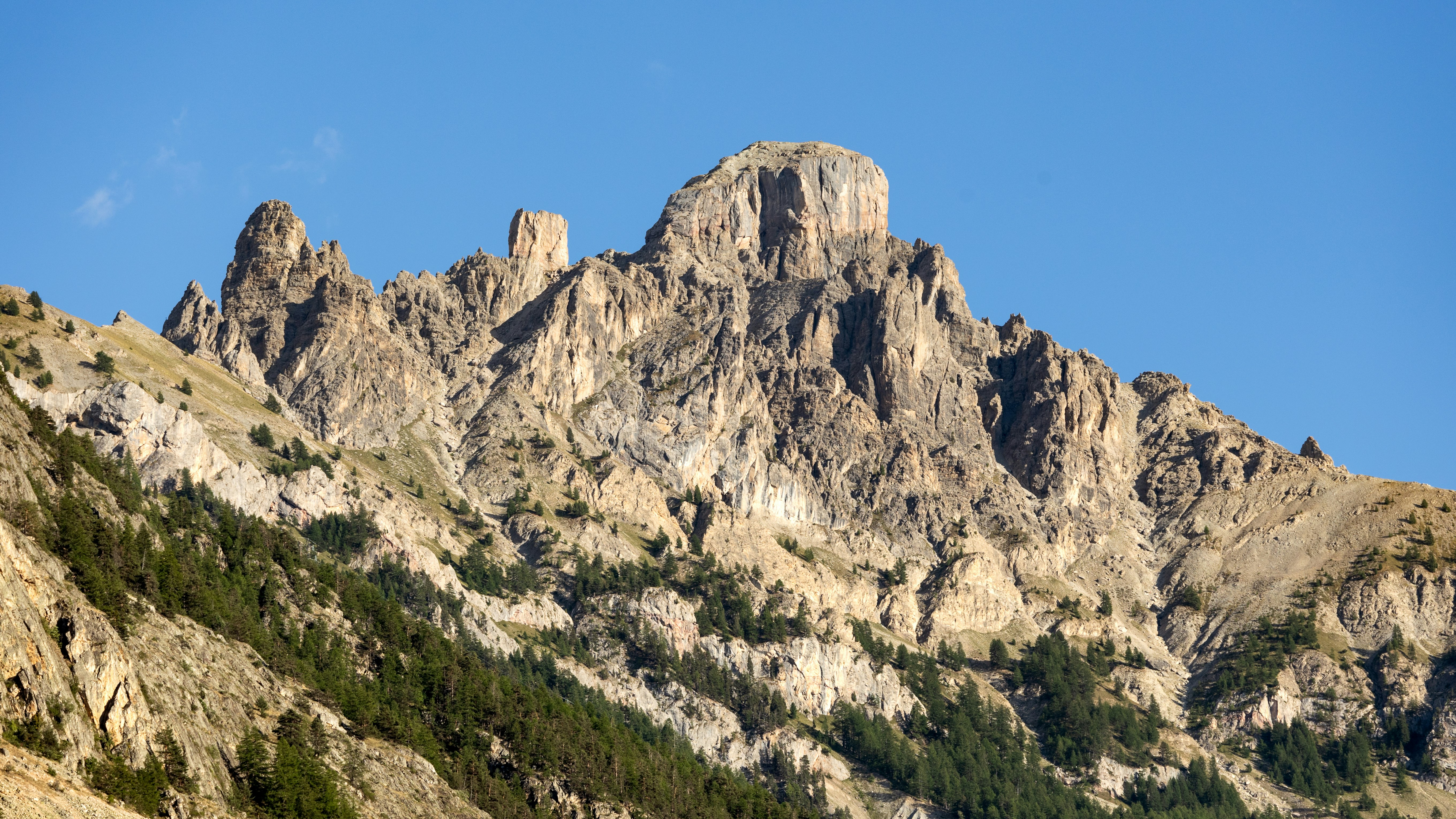 A jagged rocky mountain peak rising against a clear blue sky