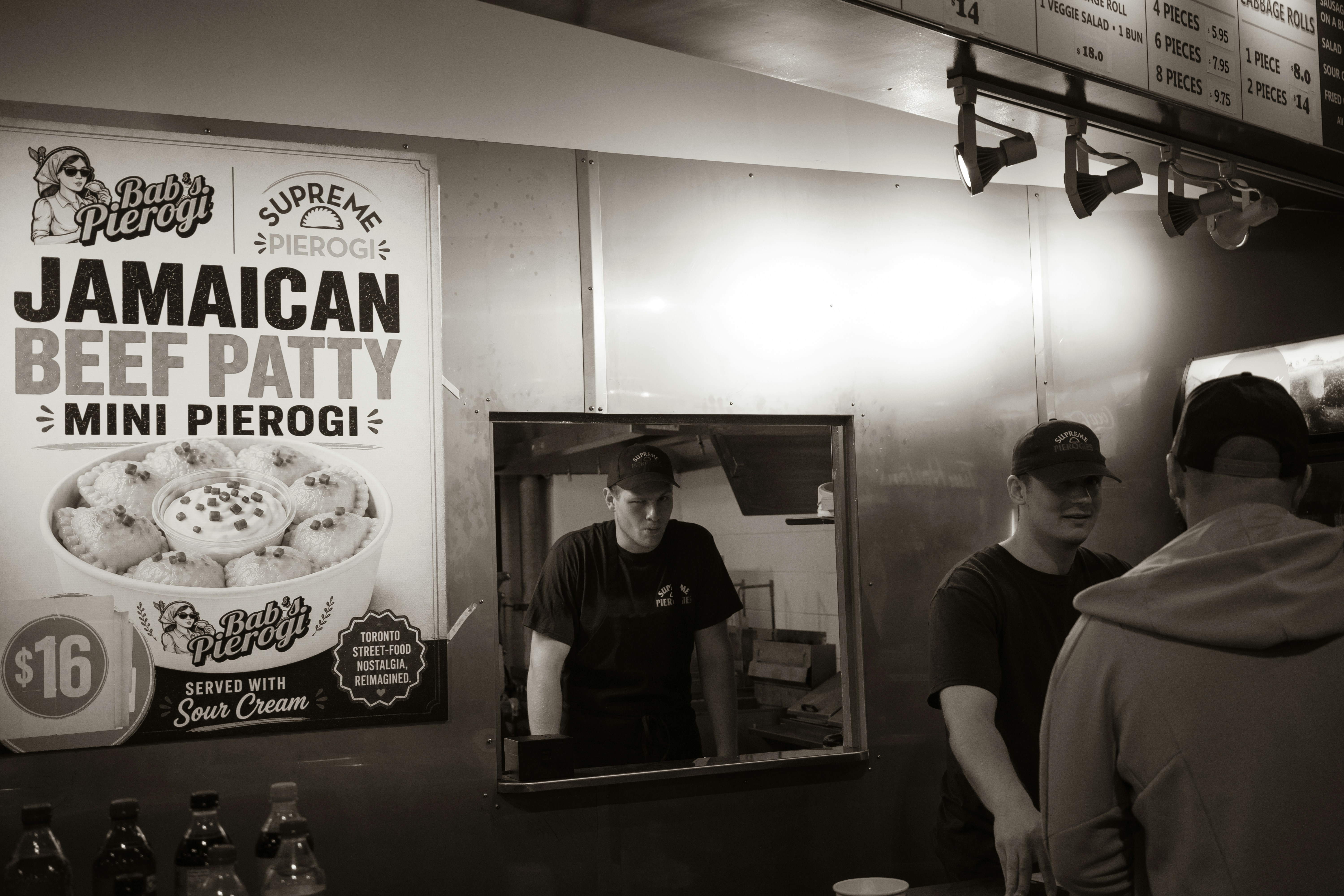 Two workers in black t-shirts and caps at a food stall counter