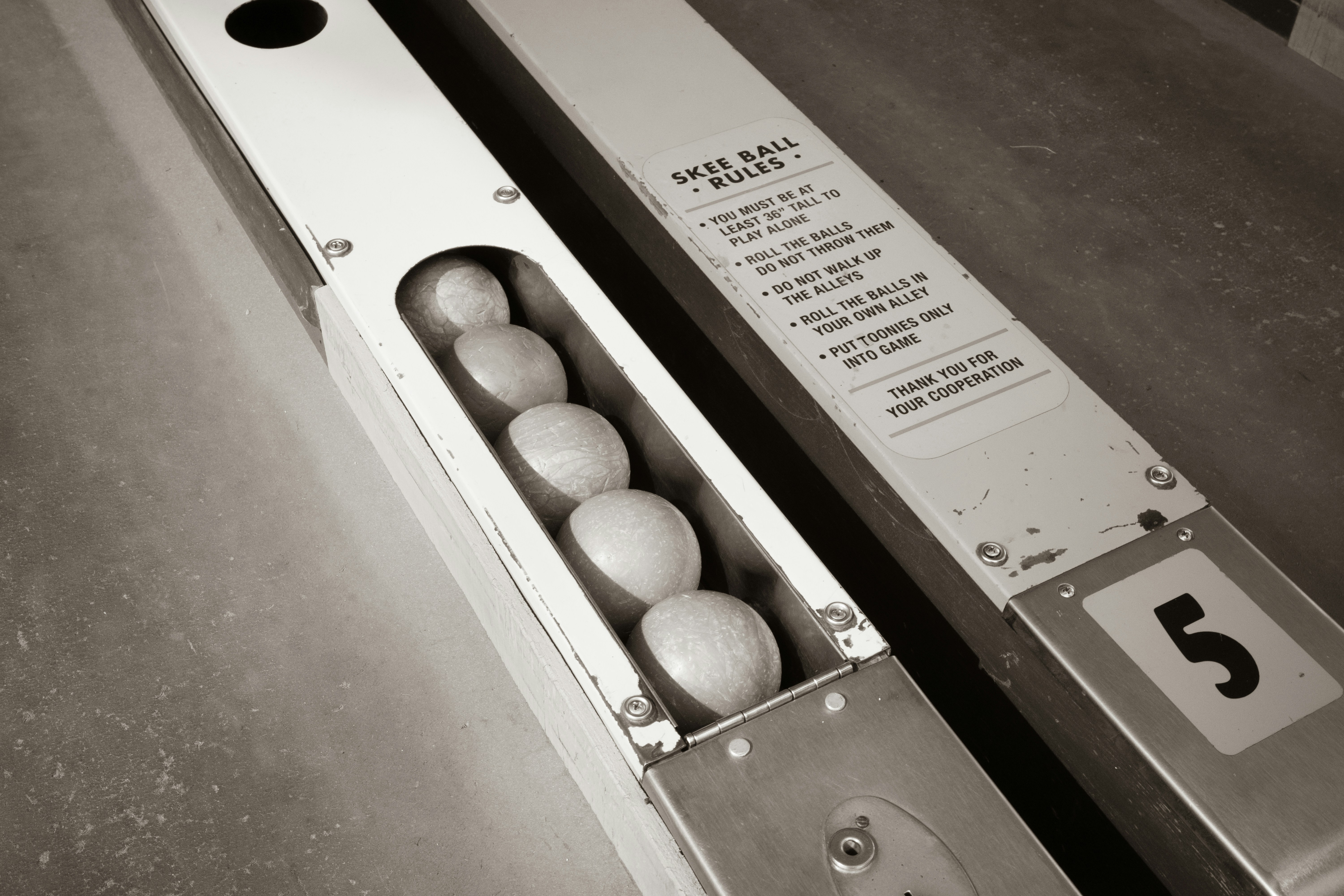 Five skee ball balls in a metal return lane with rules printed nearby