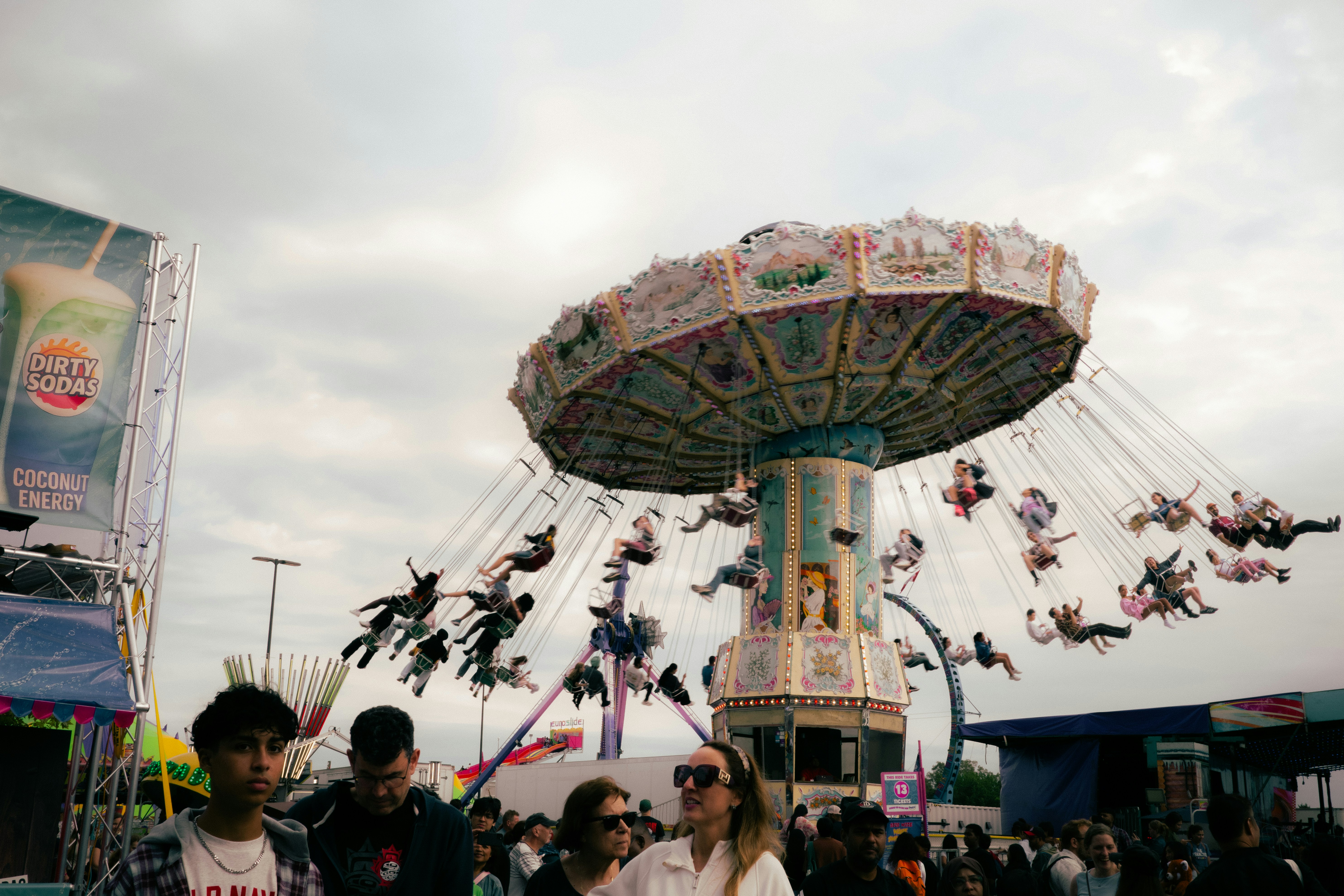 People riding a spinning swing carousel at a carnival under a cloudy sky