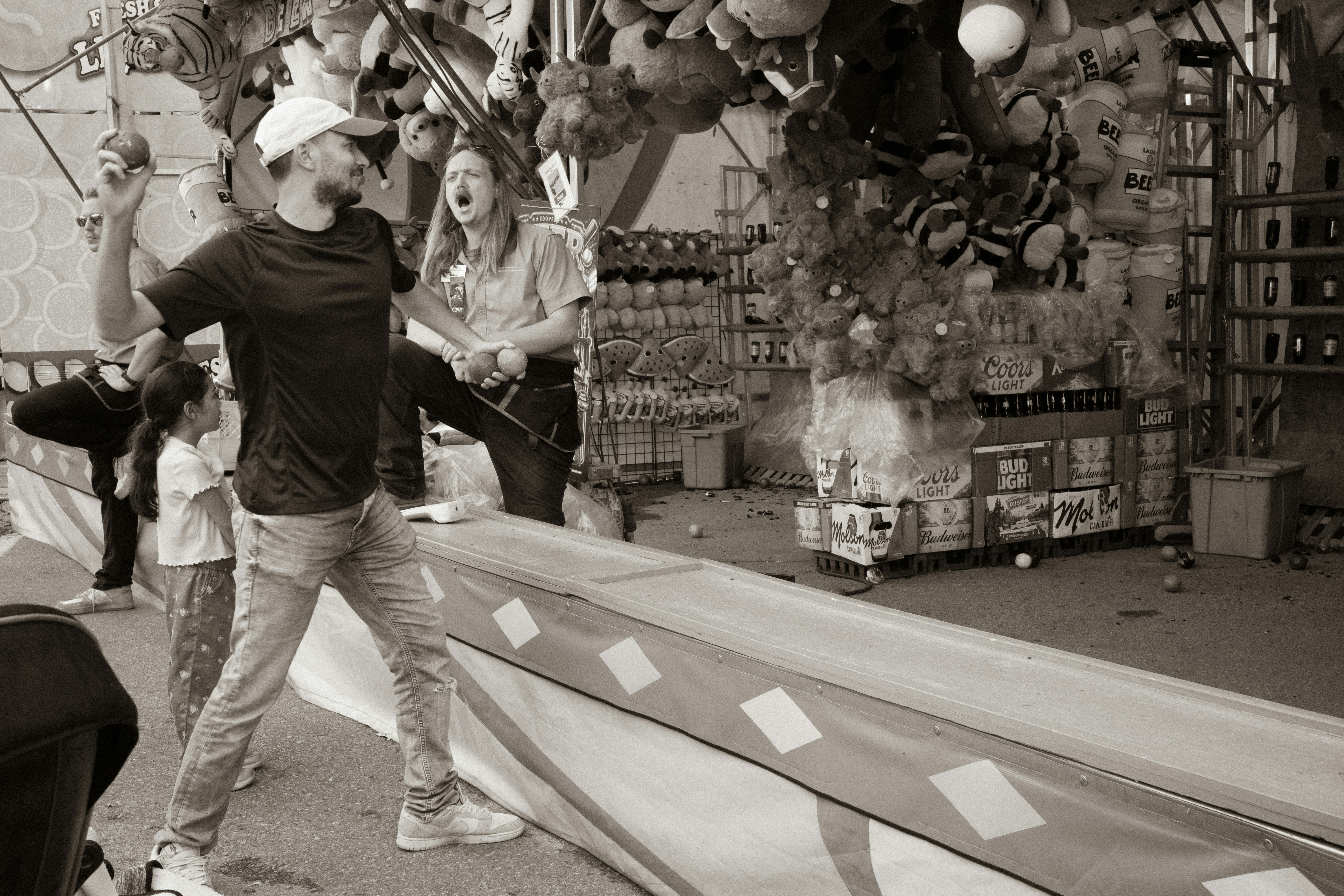 A man throwing a ball at a carnival game booth with stuffed prizes