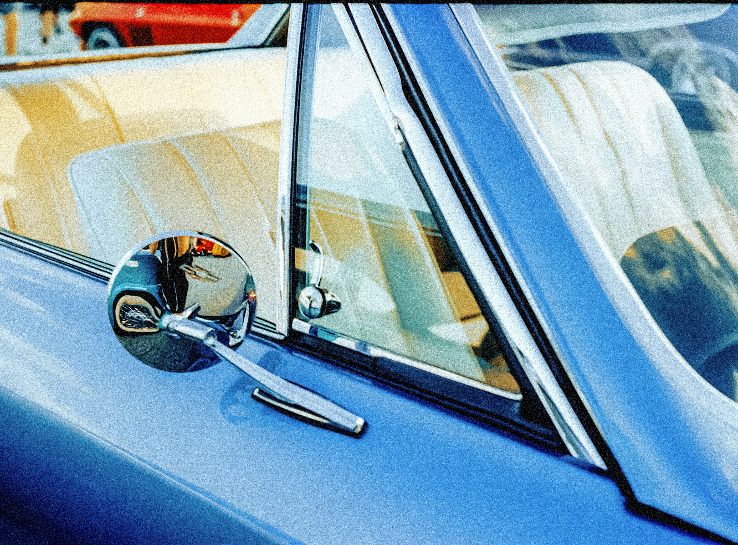 A blue vintage car with a chrome side mirror and cream interior