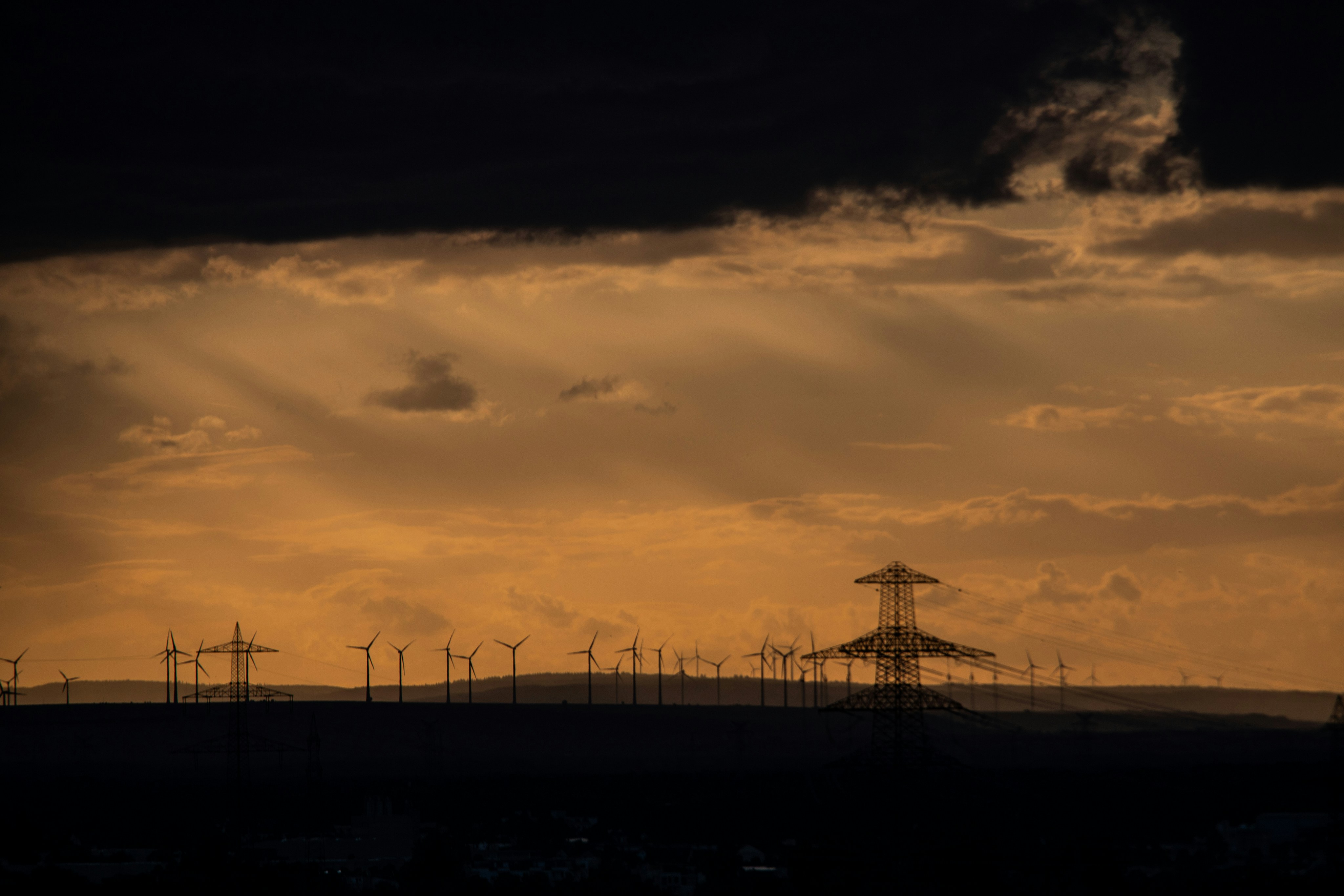 Wind turbines and electricity pylons in silhouette against a warm orange sky