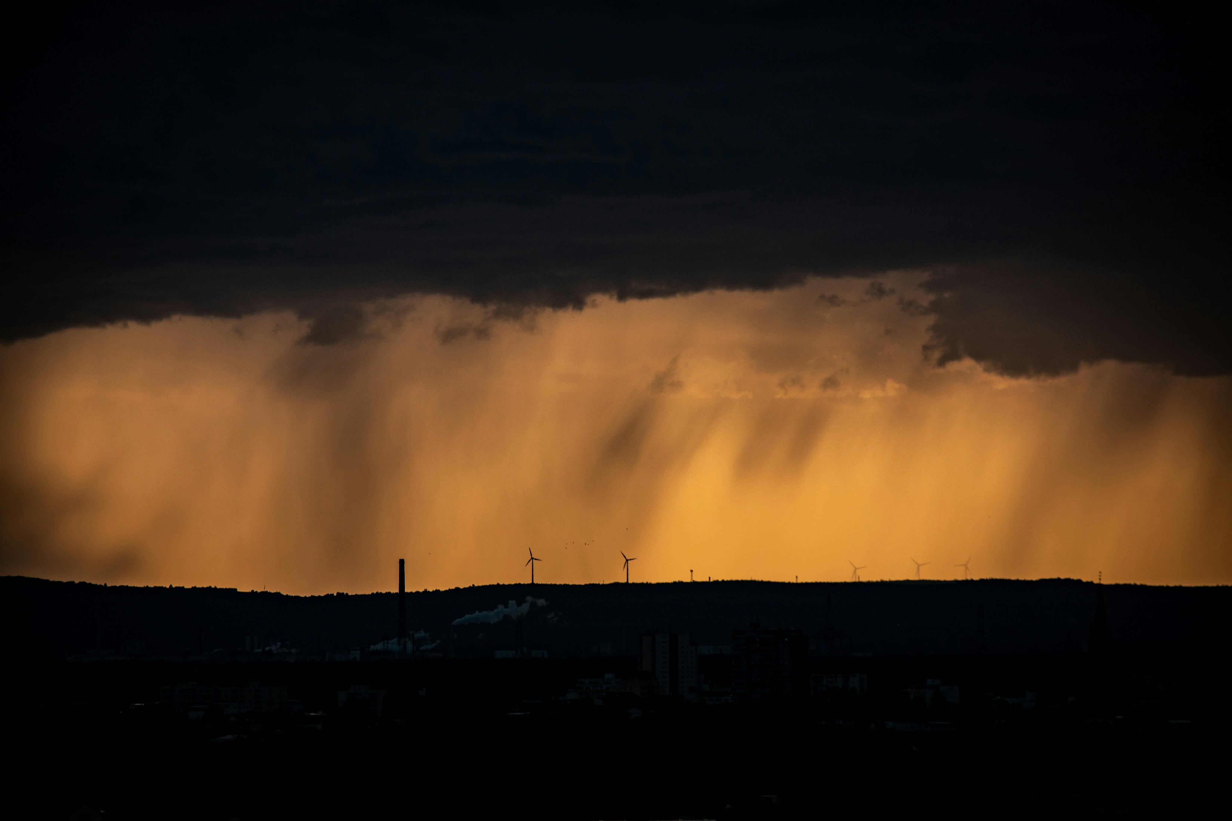 Rain falling over a dark silhouette of a landscape under a golden sky