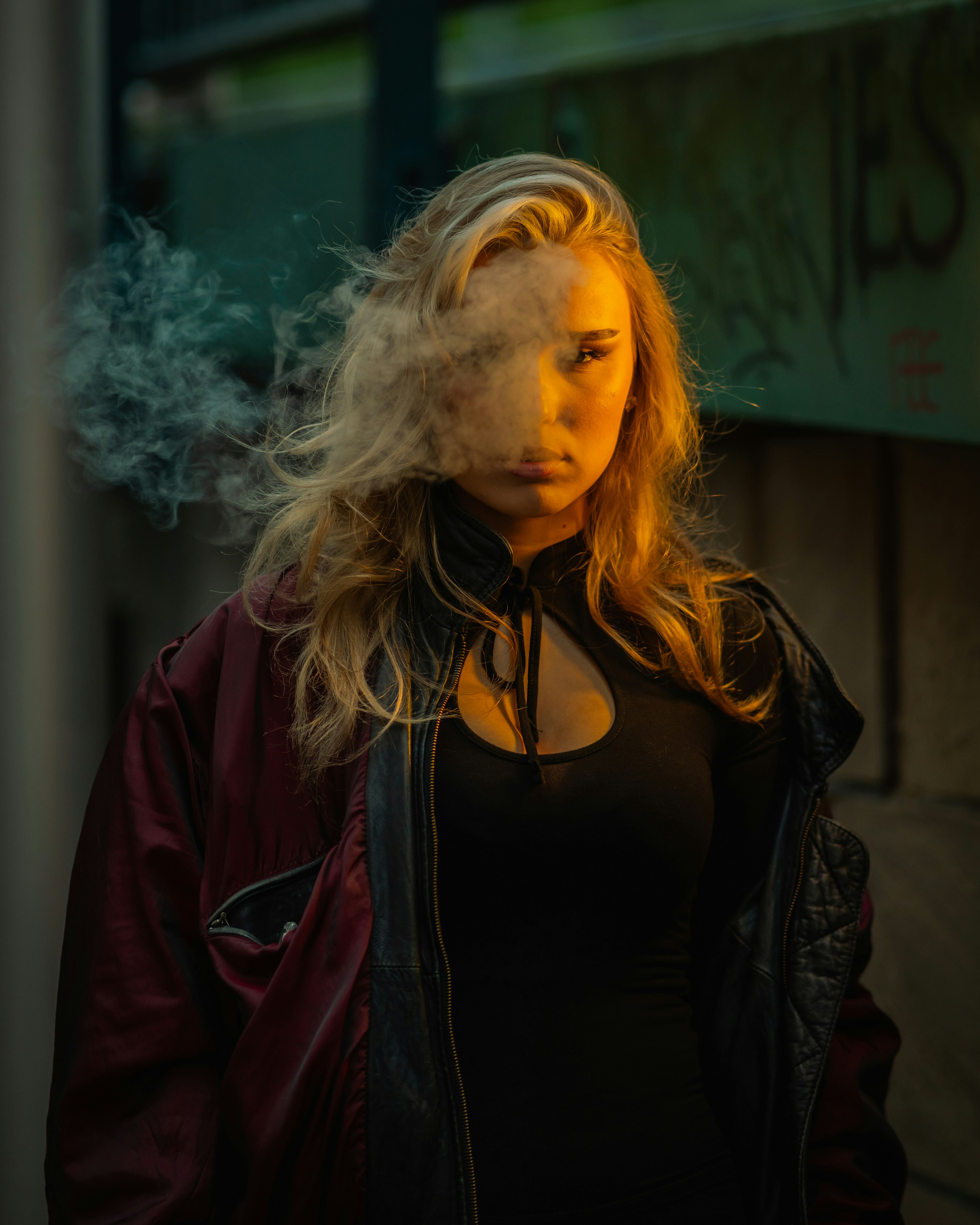 A woman in a black top and leather jacket surrounded by swirling smoke