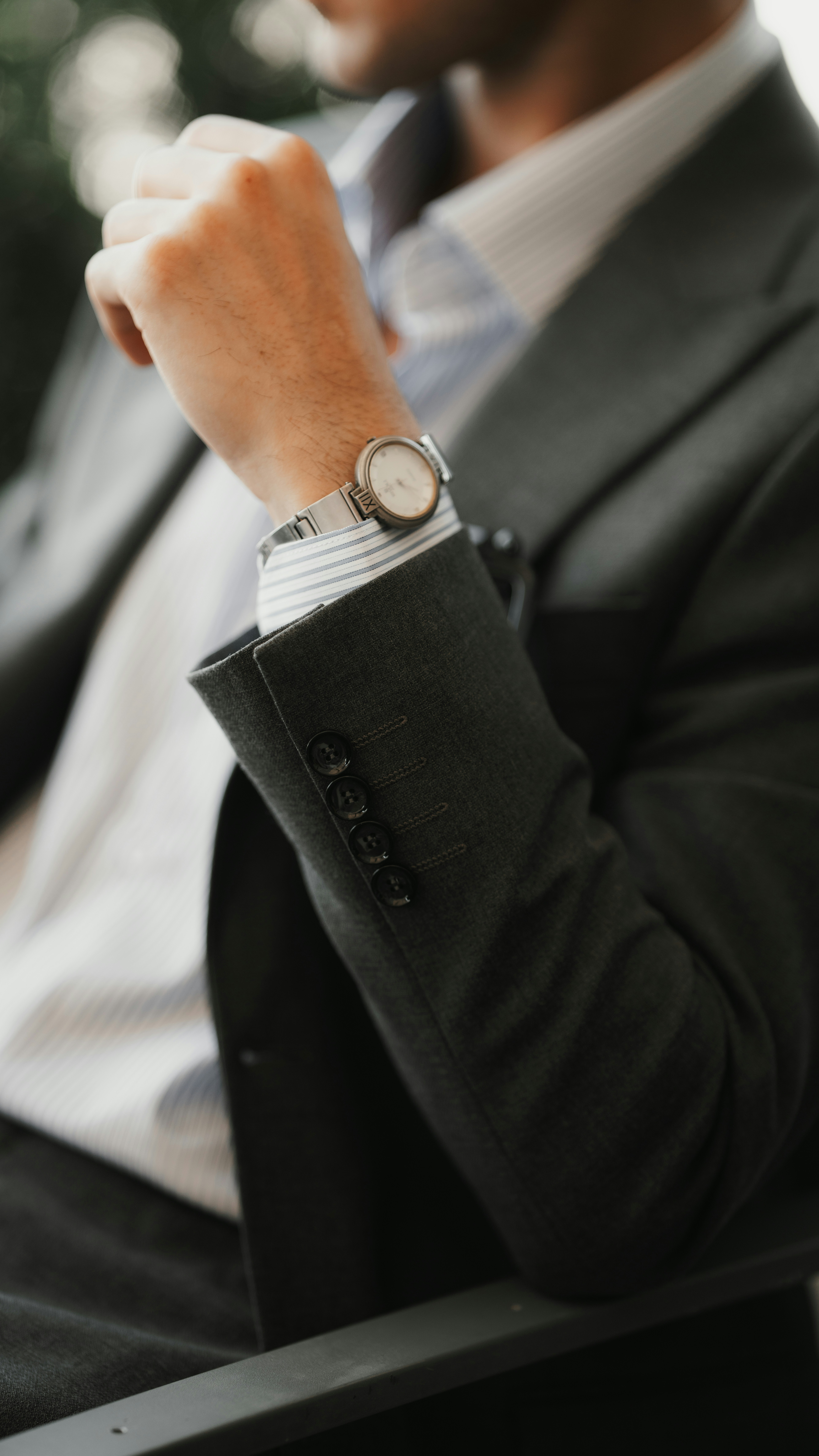A person in a dark suit and striped shirt wearing a silver wristwatch