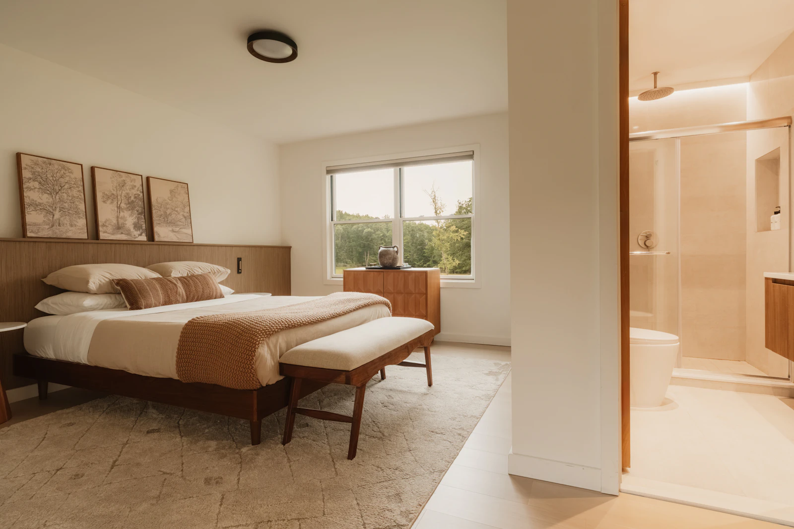Warm modern bedroom with timber furnishings, a bed, window and an adjoining bathroom containing a shower and toilet.