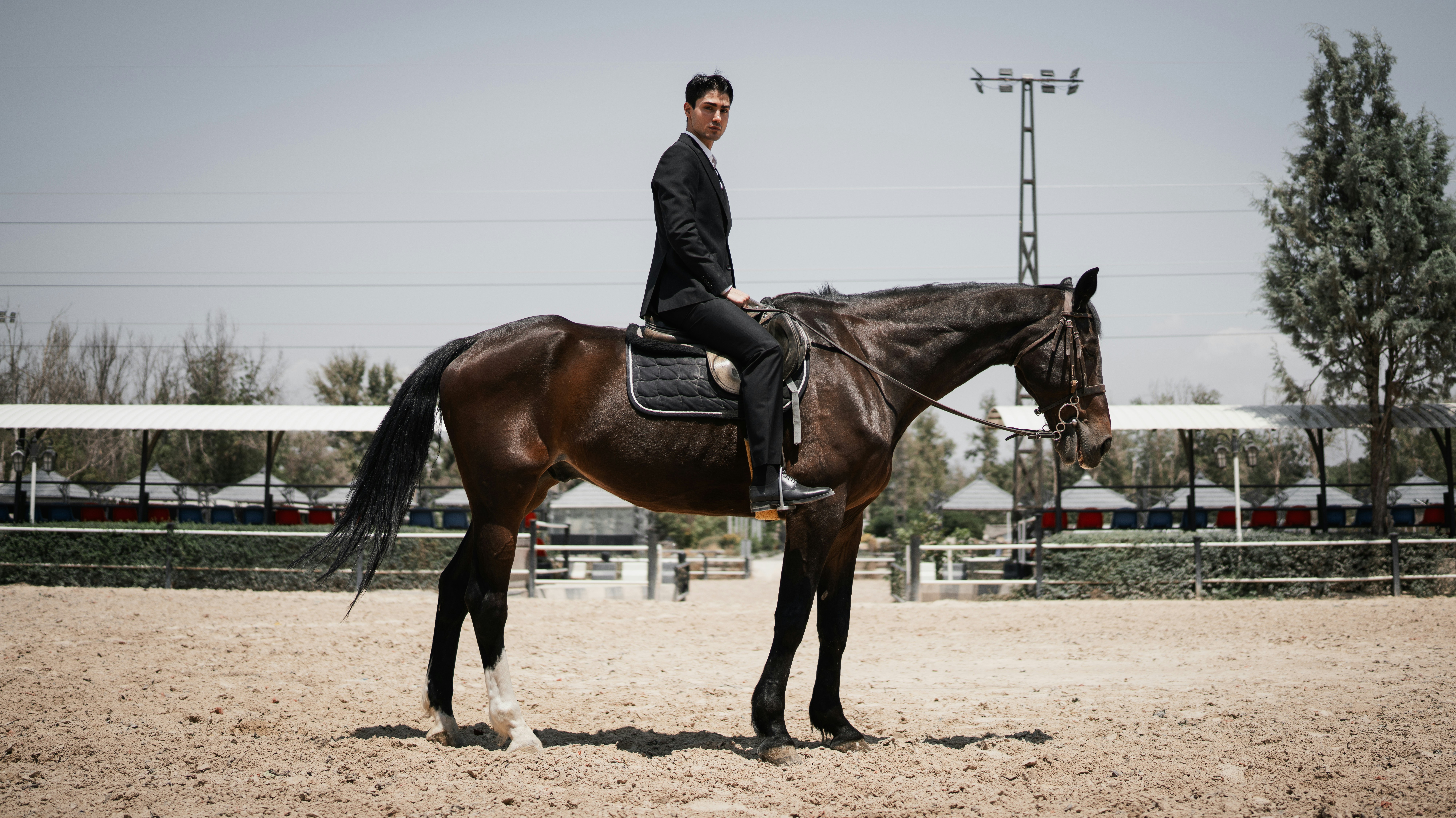 A man in a black suit riding a brown horse in an outdoor arena