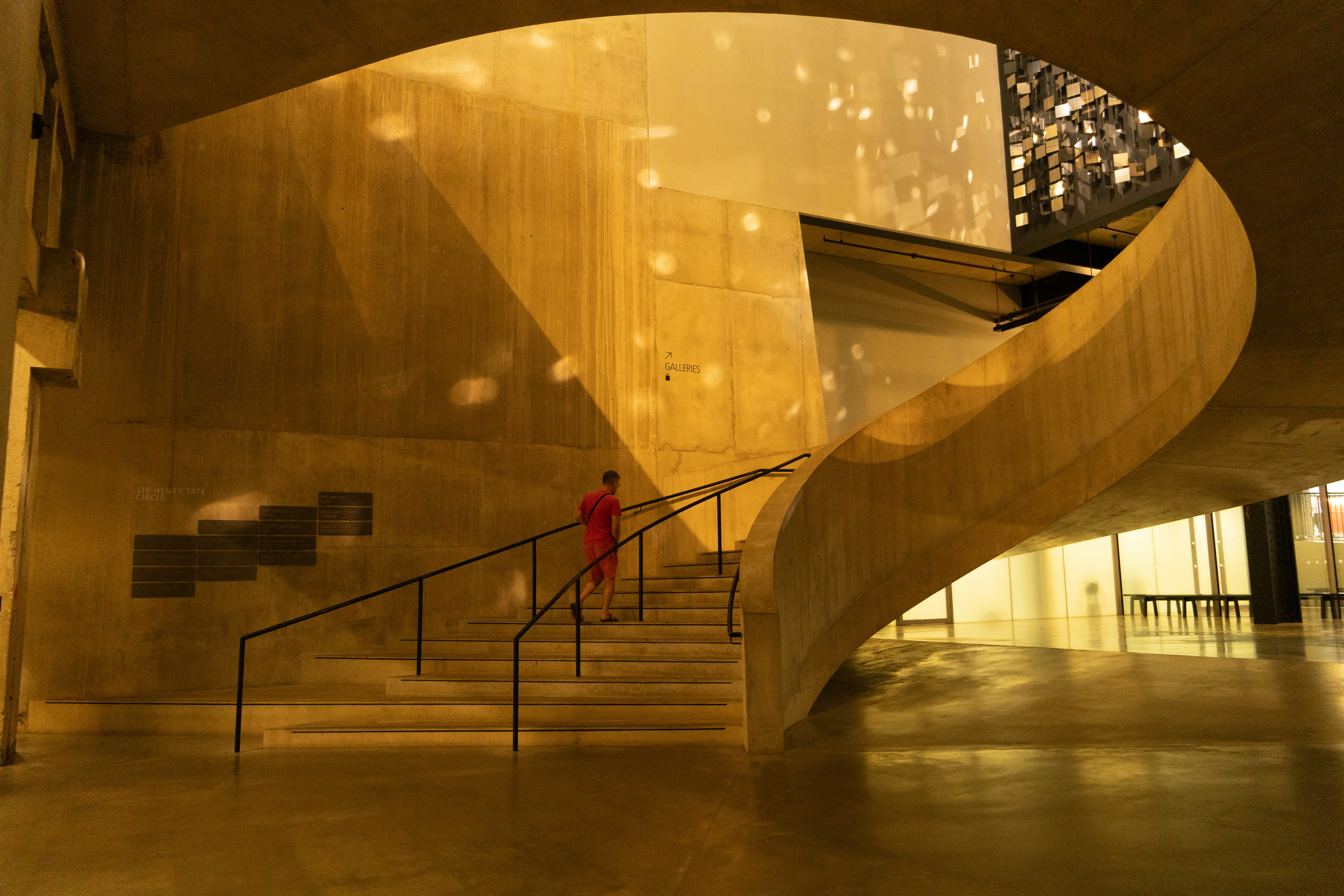 Person walking up a curved staircase in a gold-lit foyer