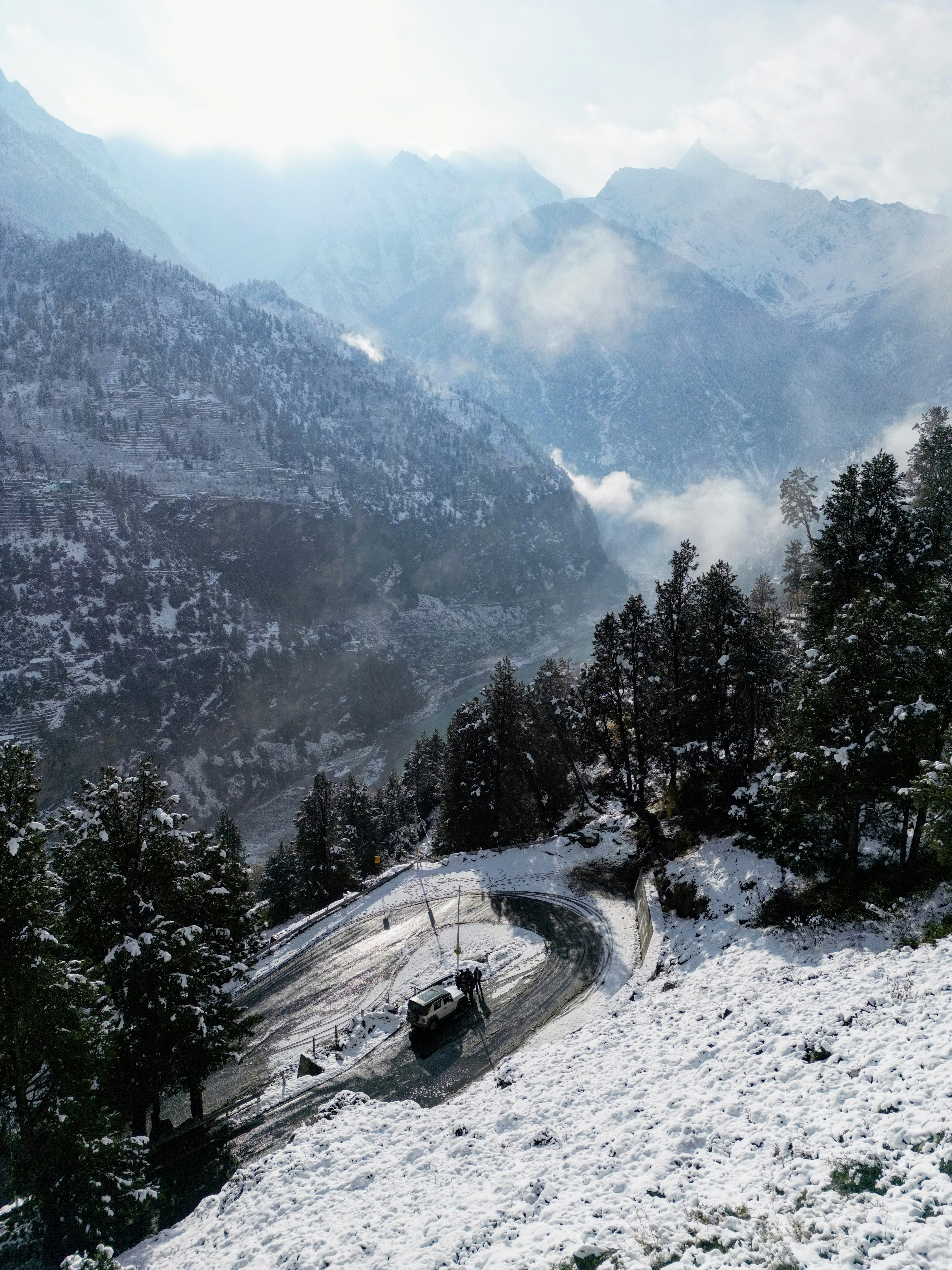A car on a winding mountain road through a snowy forest and valley