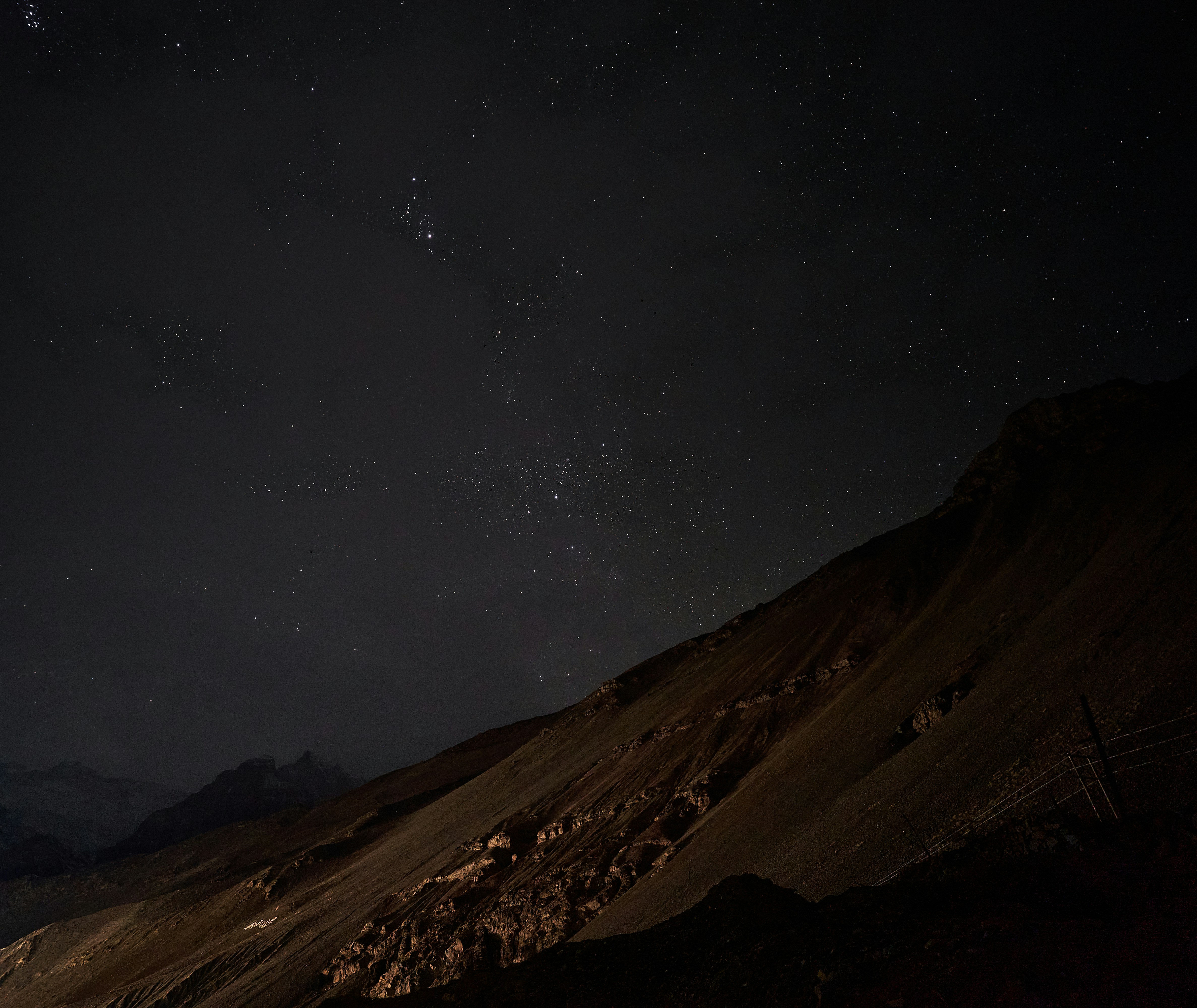 A dark mountain slope beneath a vast night sky filled with bright stars
