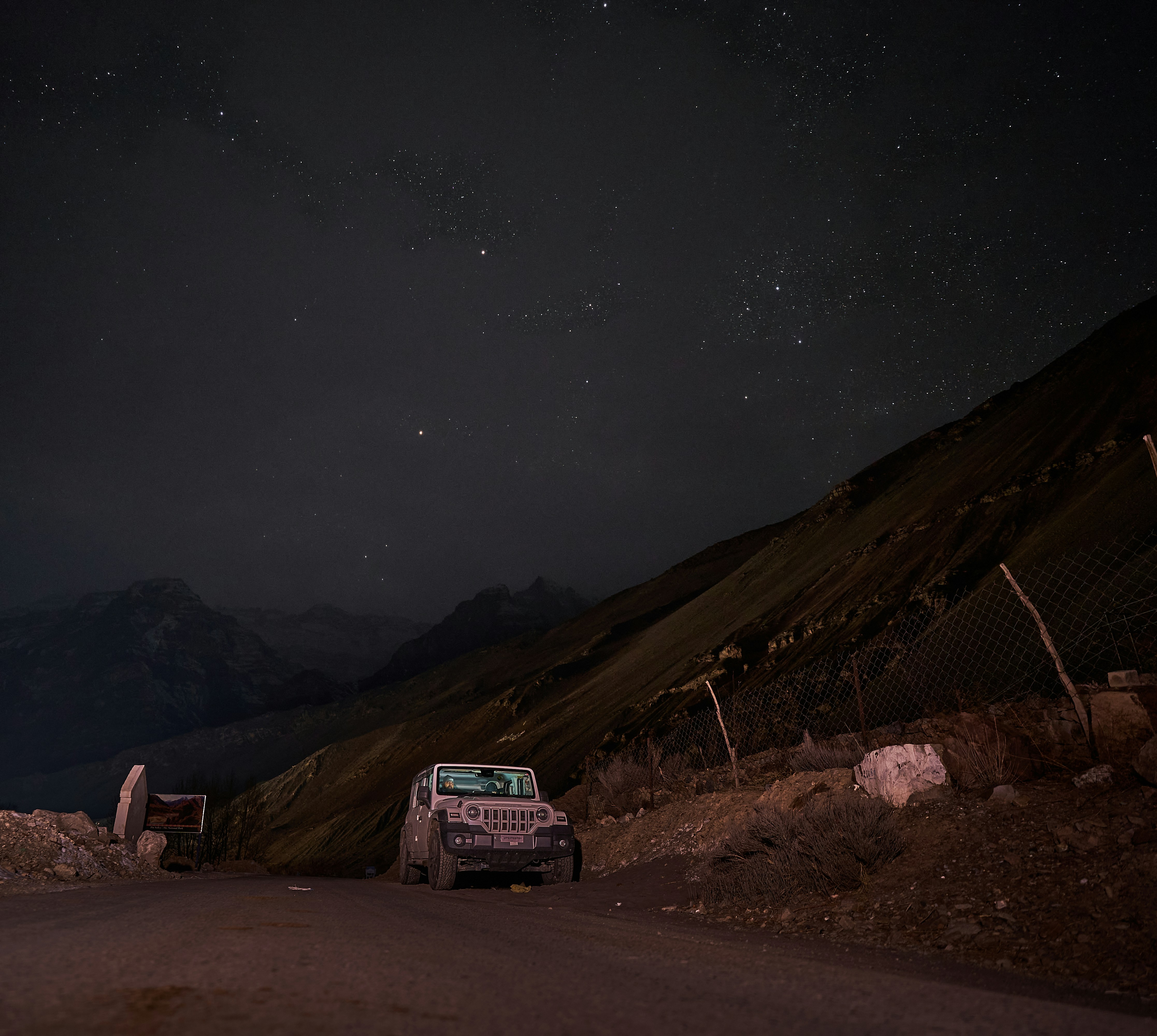 A white off-road vehicle parked on a dark mountain road under a starry sky