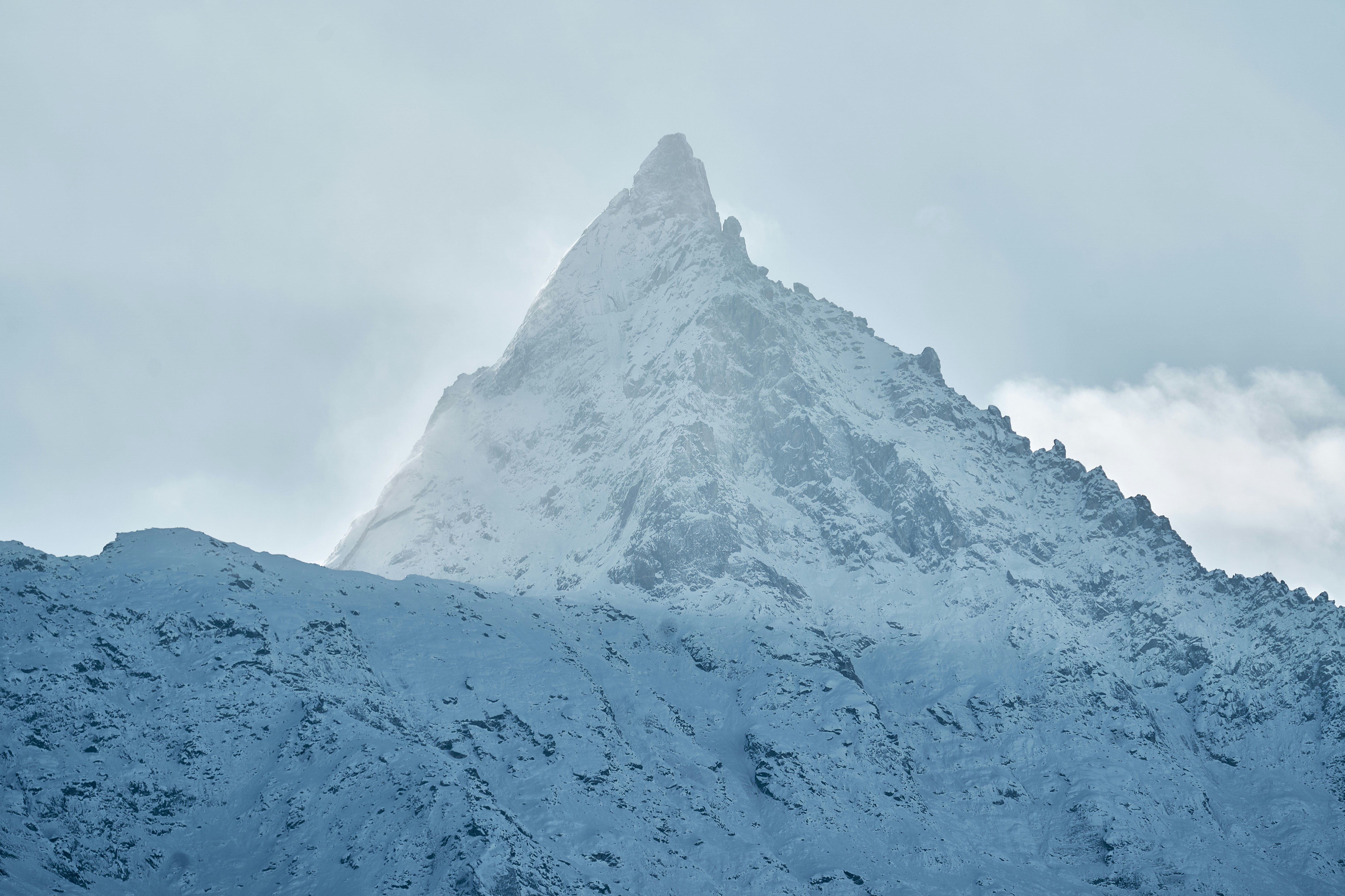 A sharp snow-covered mountain peak rising into a cloudy sky