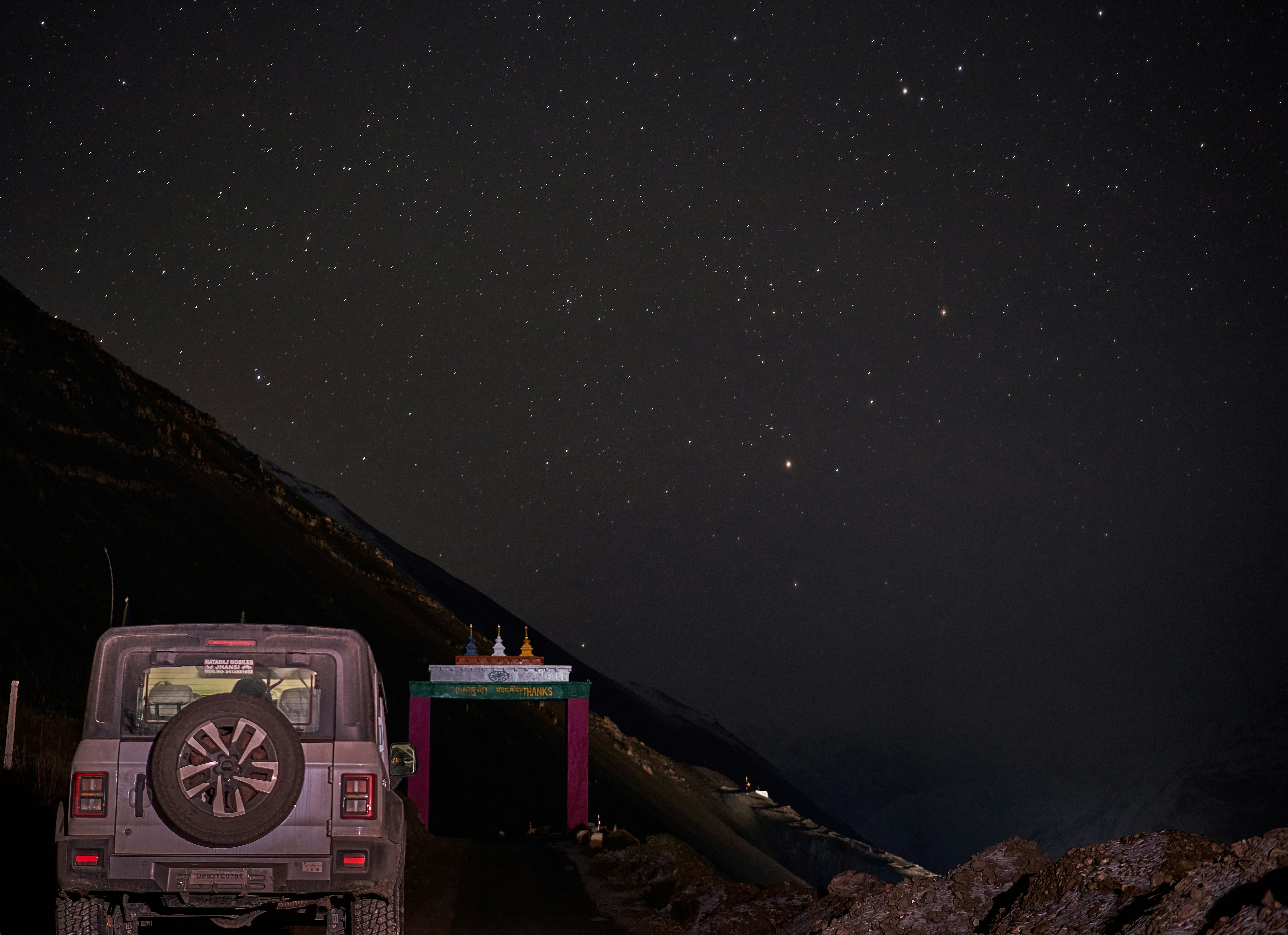 A grey off-road vehicle parked before a colorful mountain gate under a starry sky