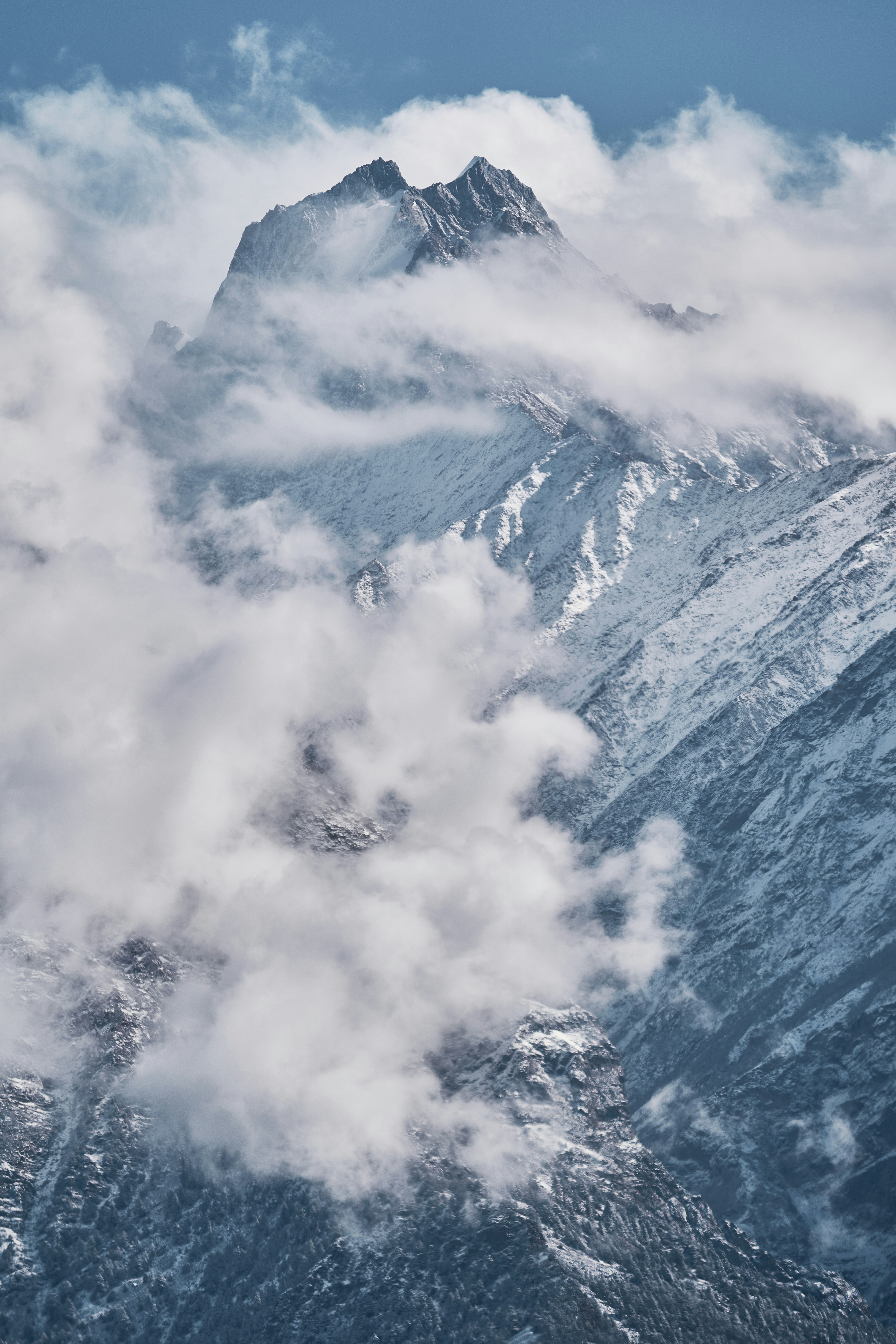 A snow-covered mountain peak partially obscured by thick white clouds