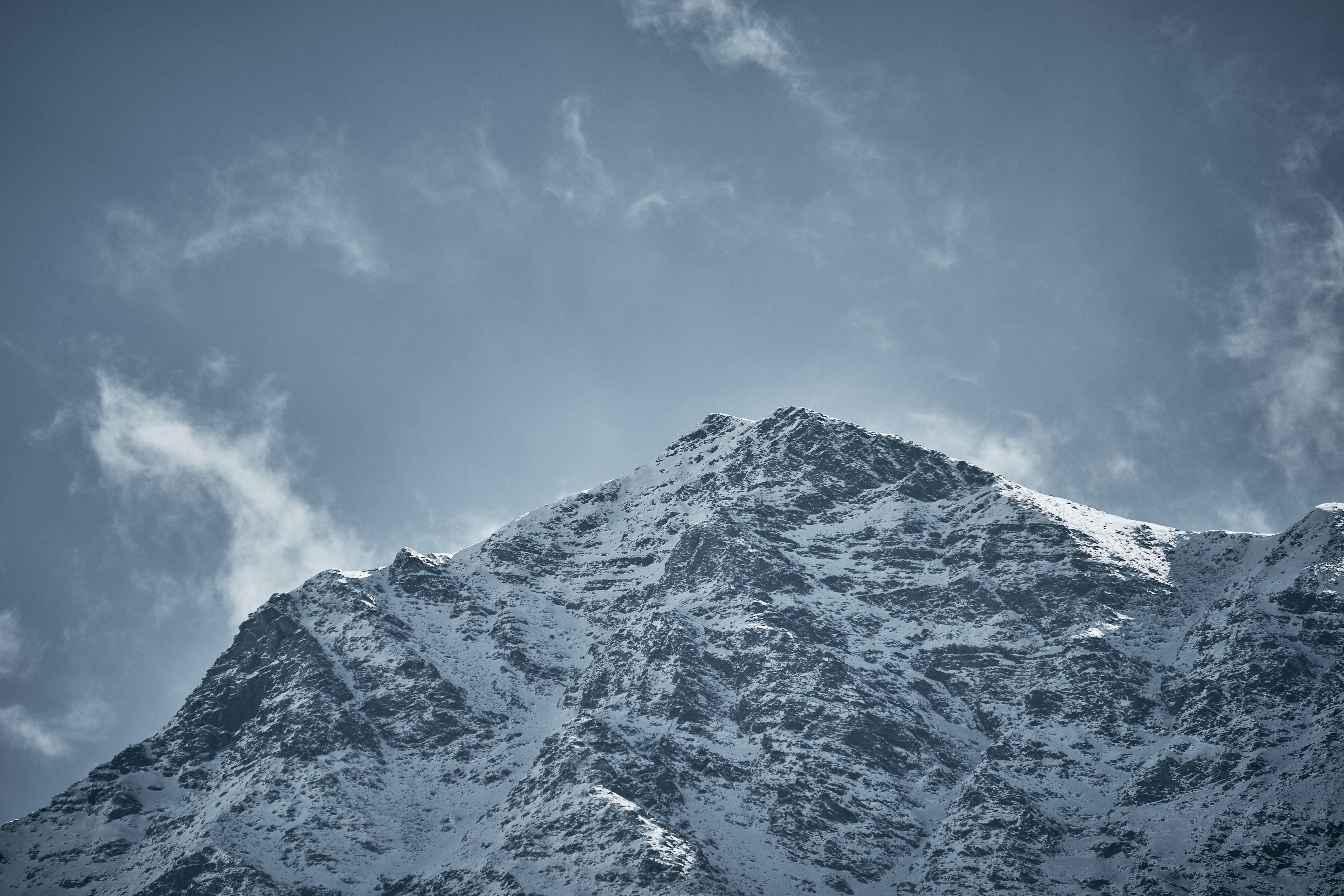 A snow-covered mountain peak against a cloudy blue sky