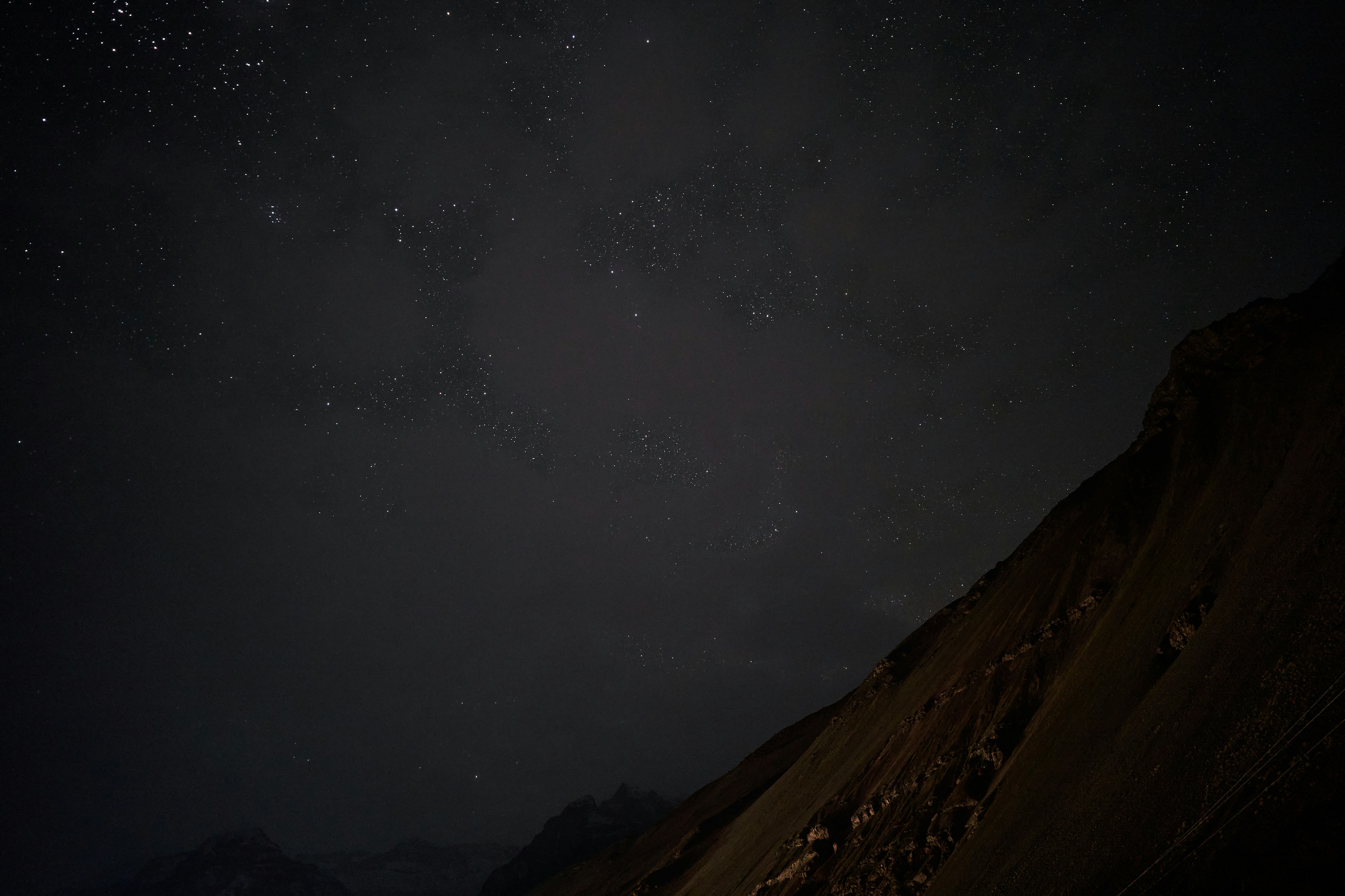 A dark mountain slope beneath a vast night sky filled with scattered stars