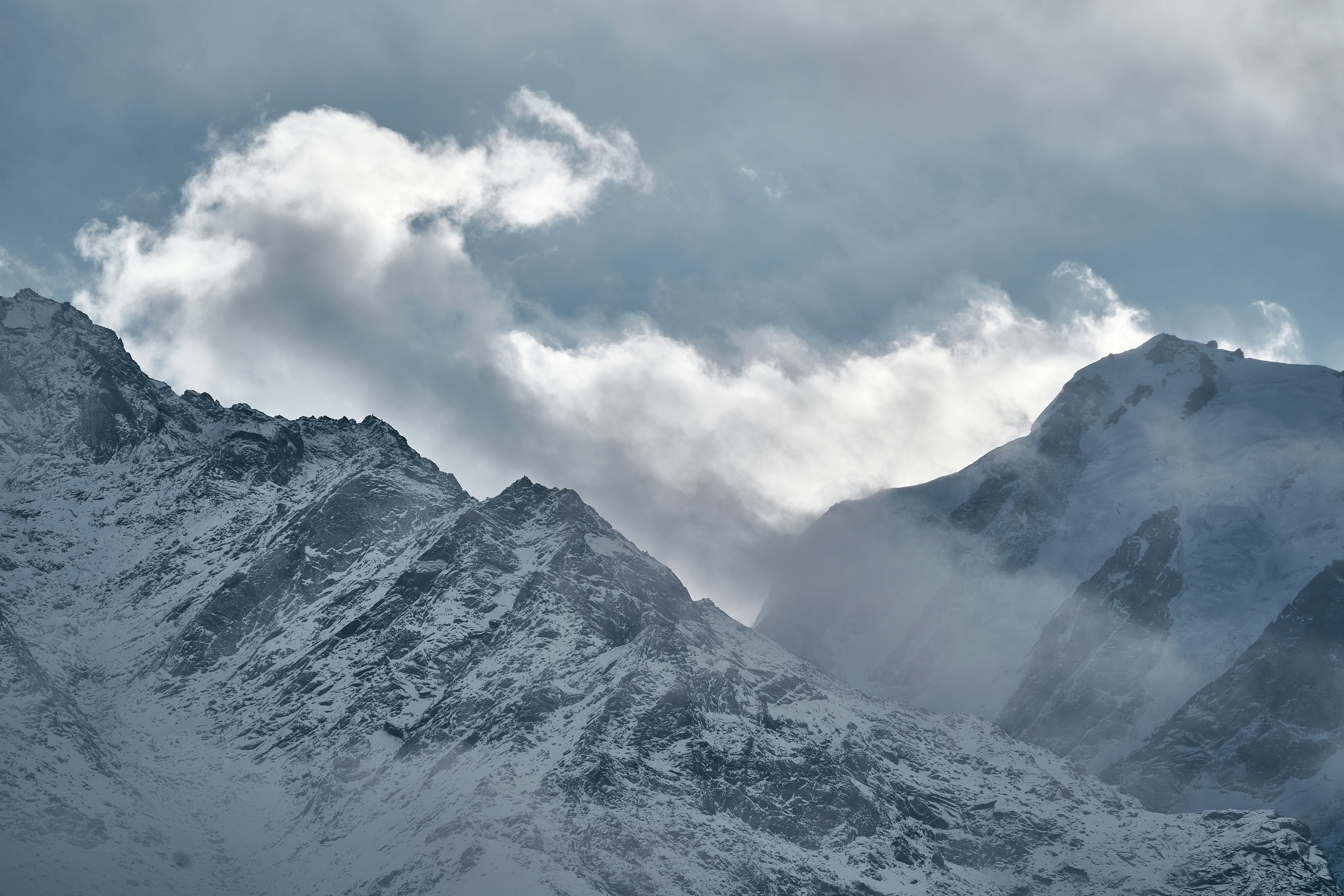 Snow-covered mountain peaks partially obscured by thick clouds under a bright sky