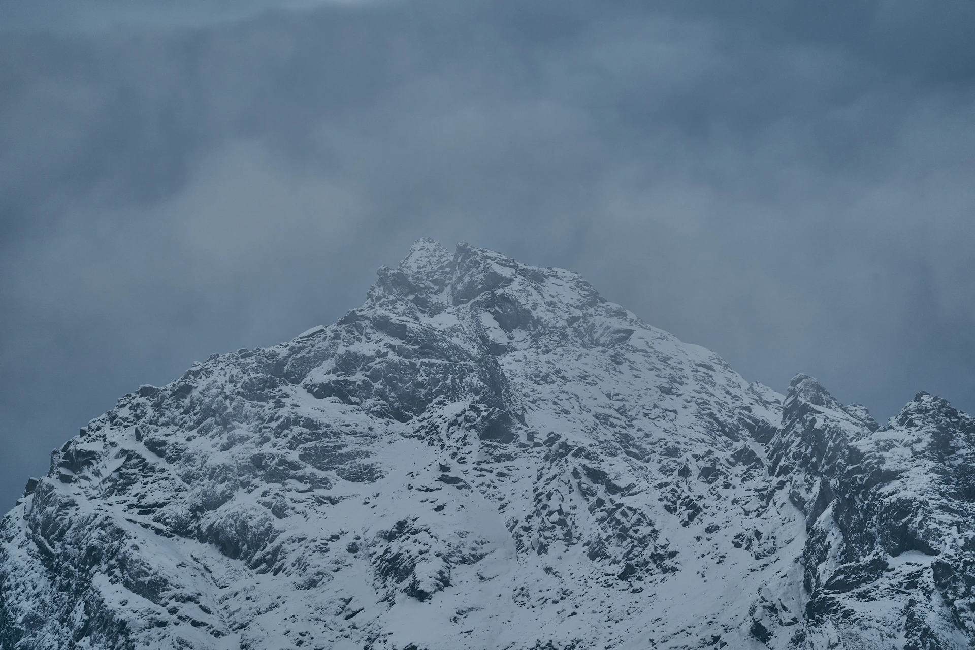 A snow covered mountain peak under a dark and cloudy sky