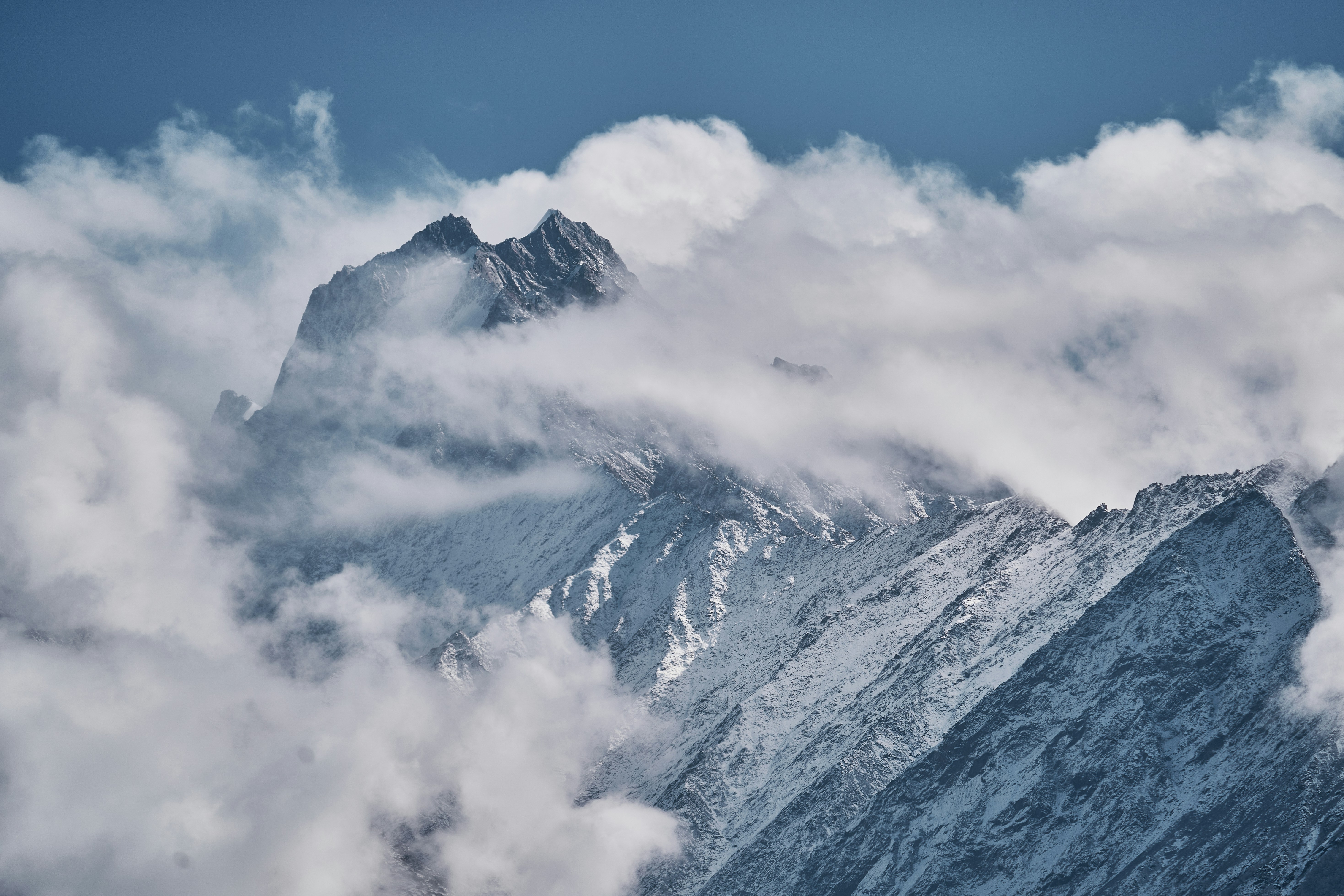 A snow-covered mountain peak partially obscured by thick white clouds