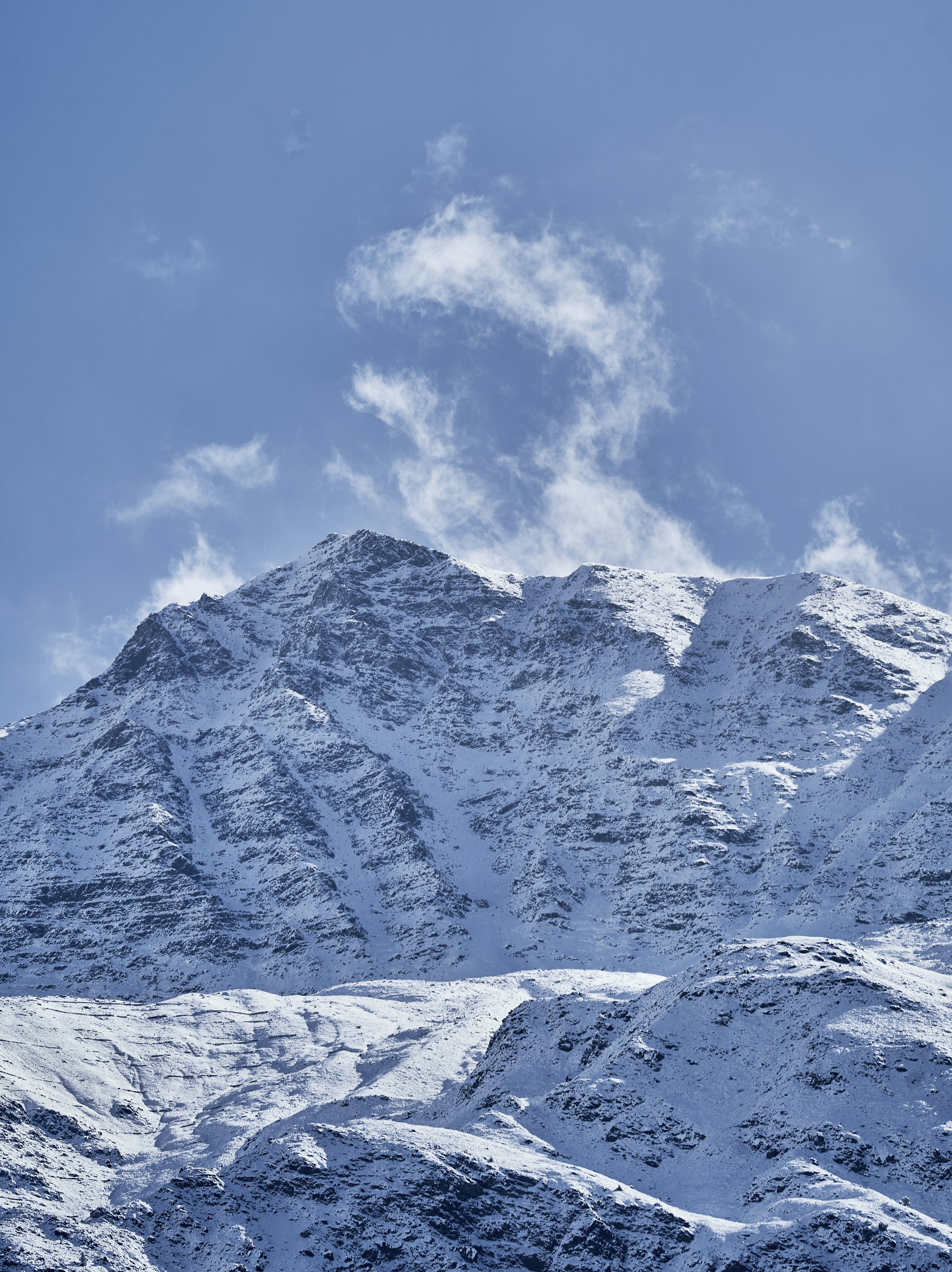 A snow covered mountain peak under a clear blue sky with wispy clouds