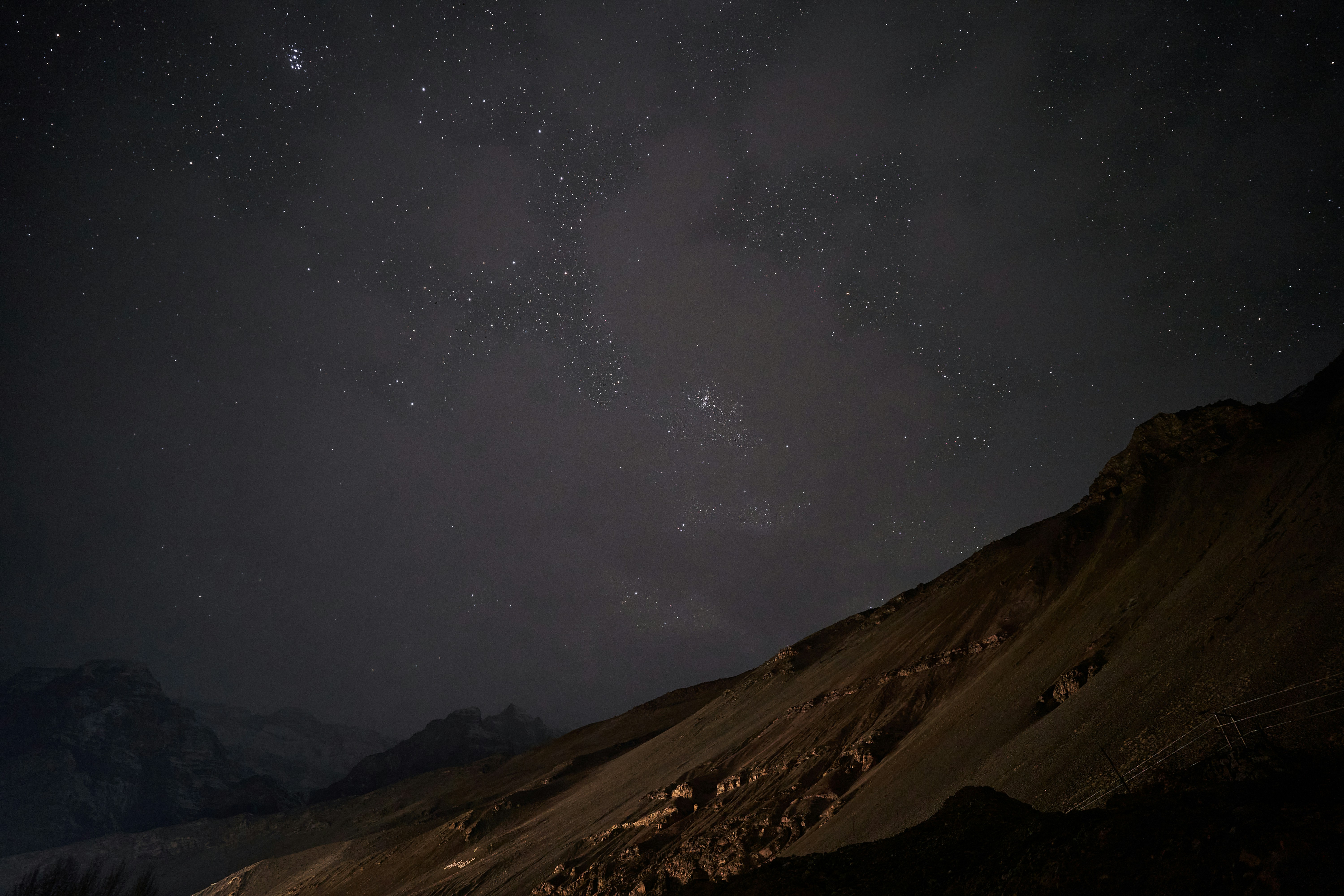 A dark night sky filled with stars above a rugged mountain slope