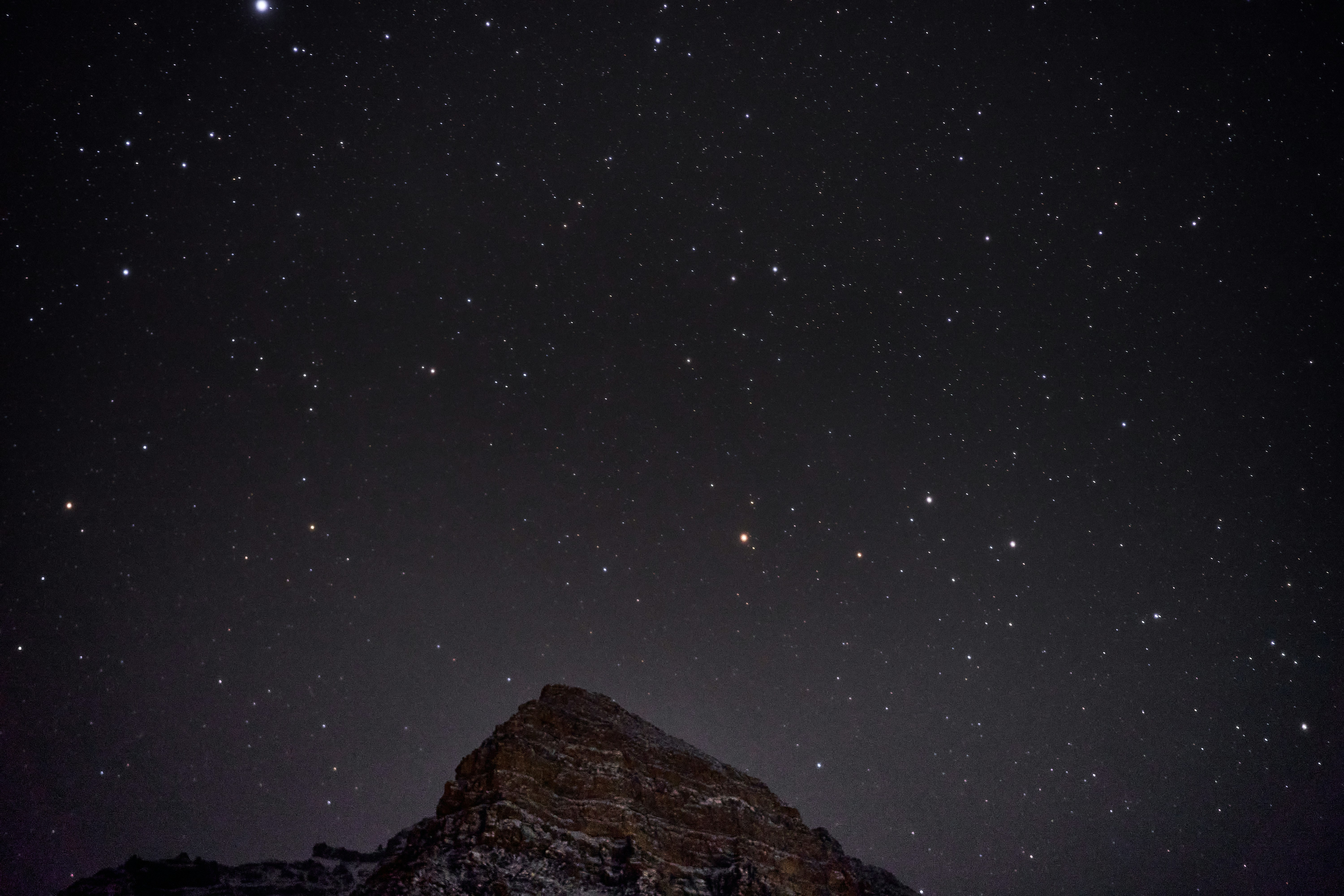 A rocky mountain peak under a vast night sky filled with bright stars