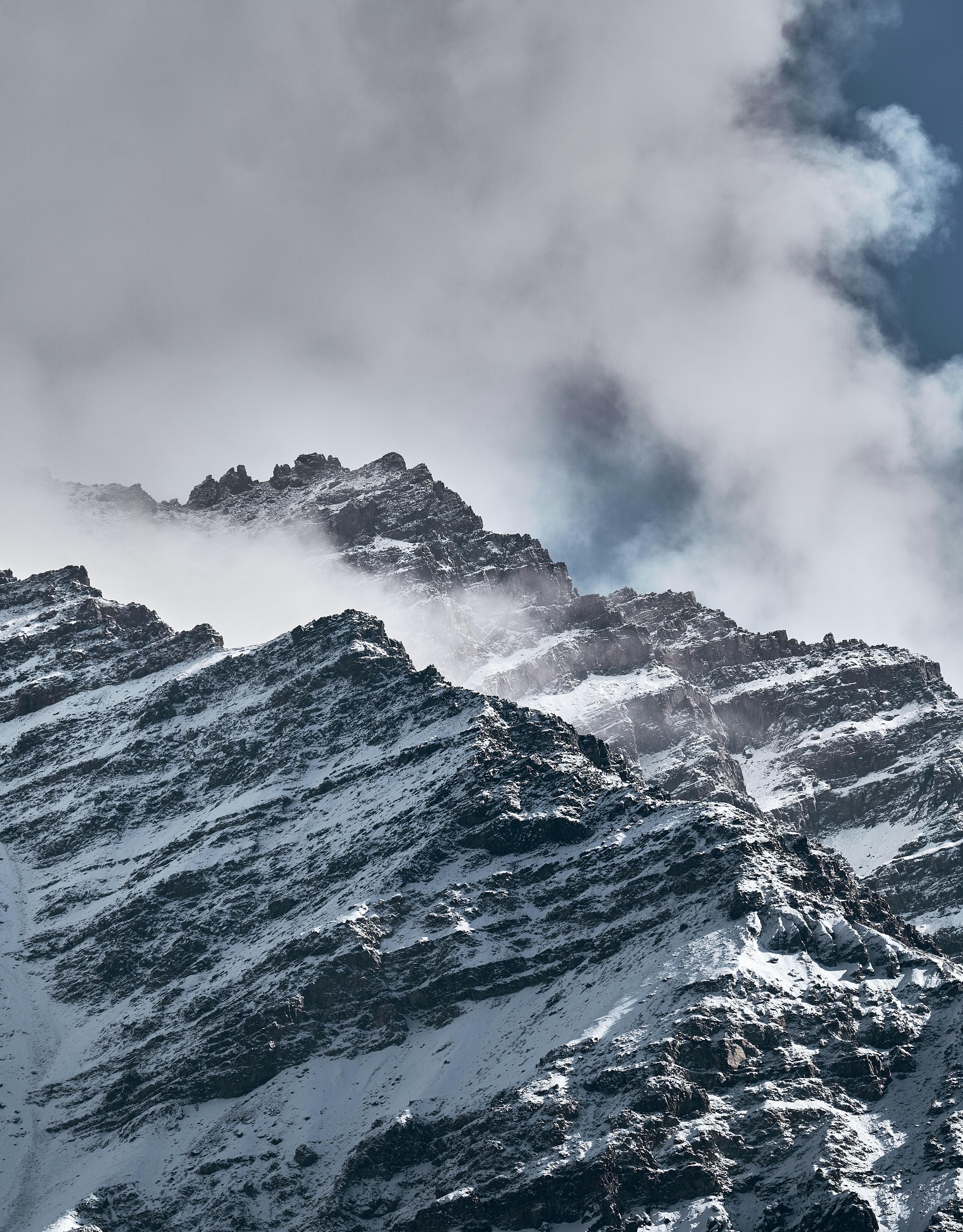 Snowy mountain peaks partially obscured by thick white clouds against a blue sky