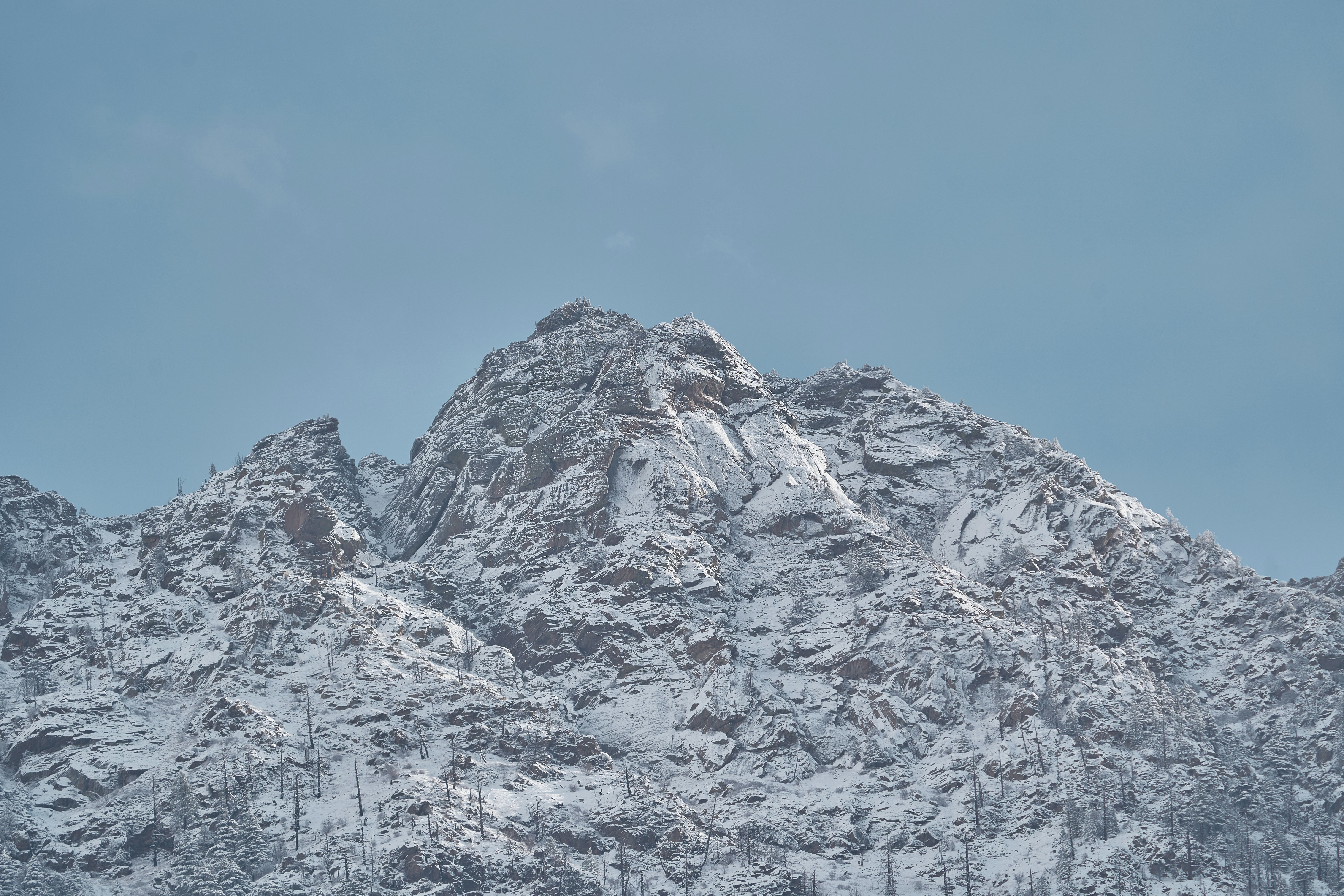 A jagged mountain peak covered in snow against a clear blue sky
