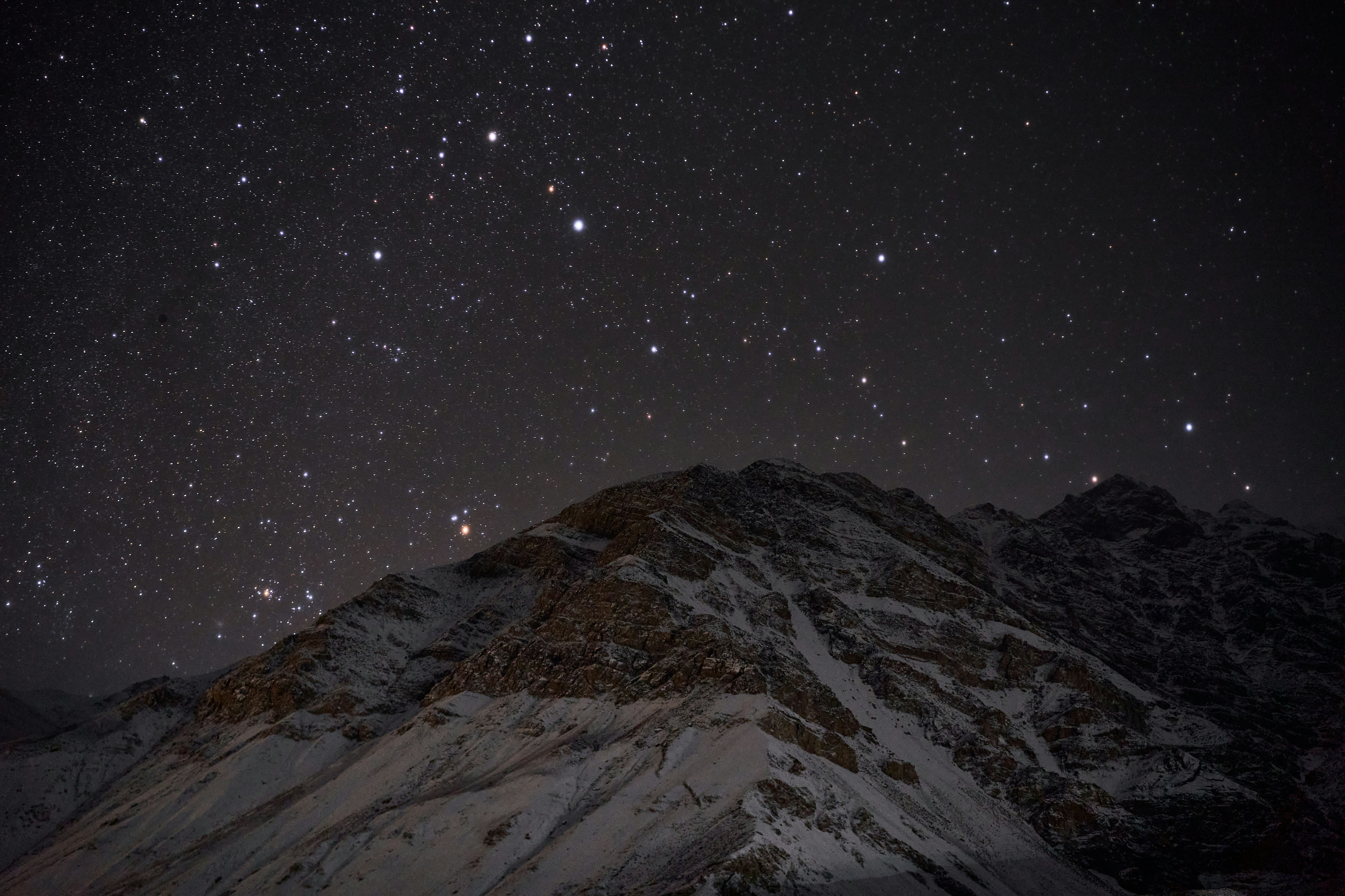 A snow-covered mountain peak under a dark night sky filled with bright stars