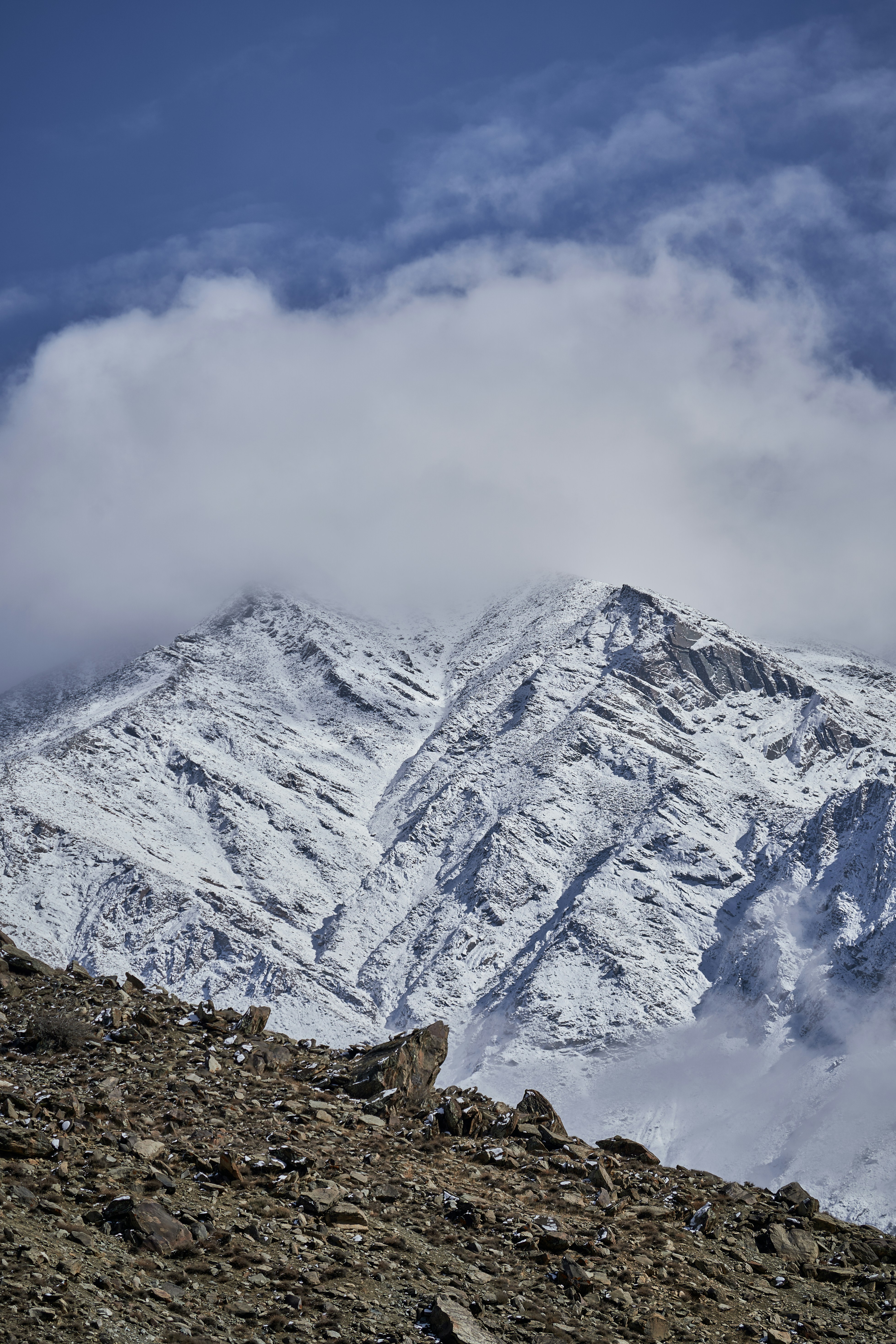 Snow covered mountain peak under a thick layer of clouds above rocky terrain