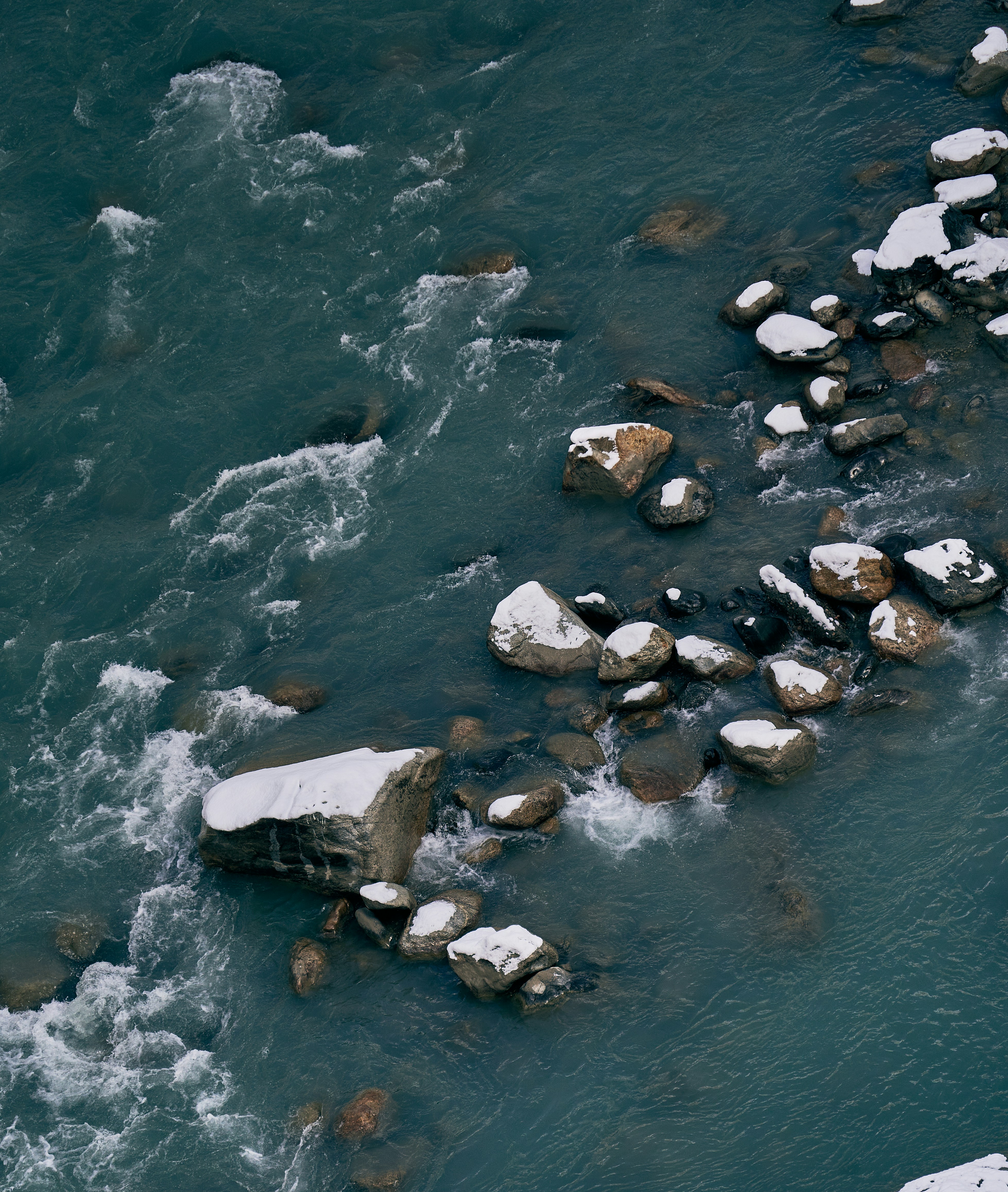 Snow-dusted rocks in a fast-flowing river with dark blue water