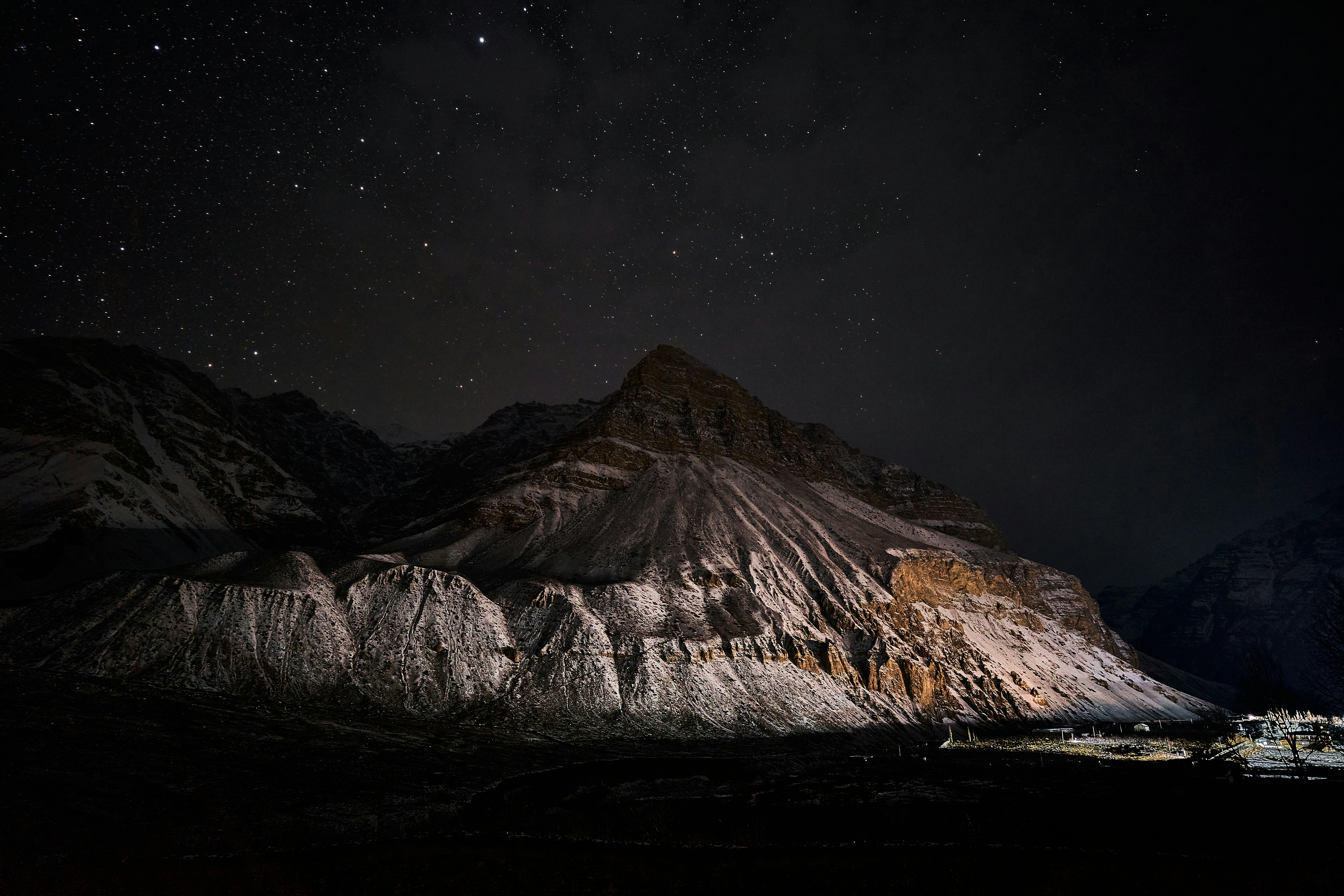 A snow-dusted mountain peak under a dark night sky filled with bright stars