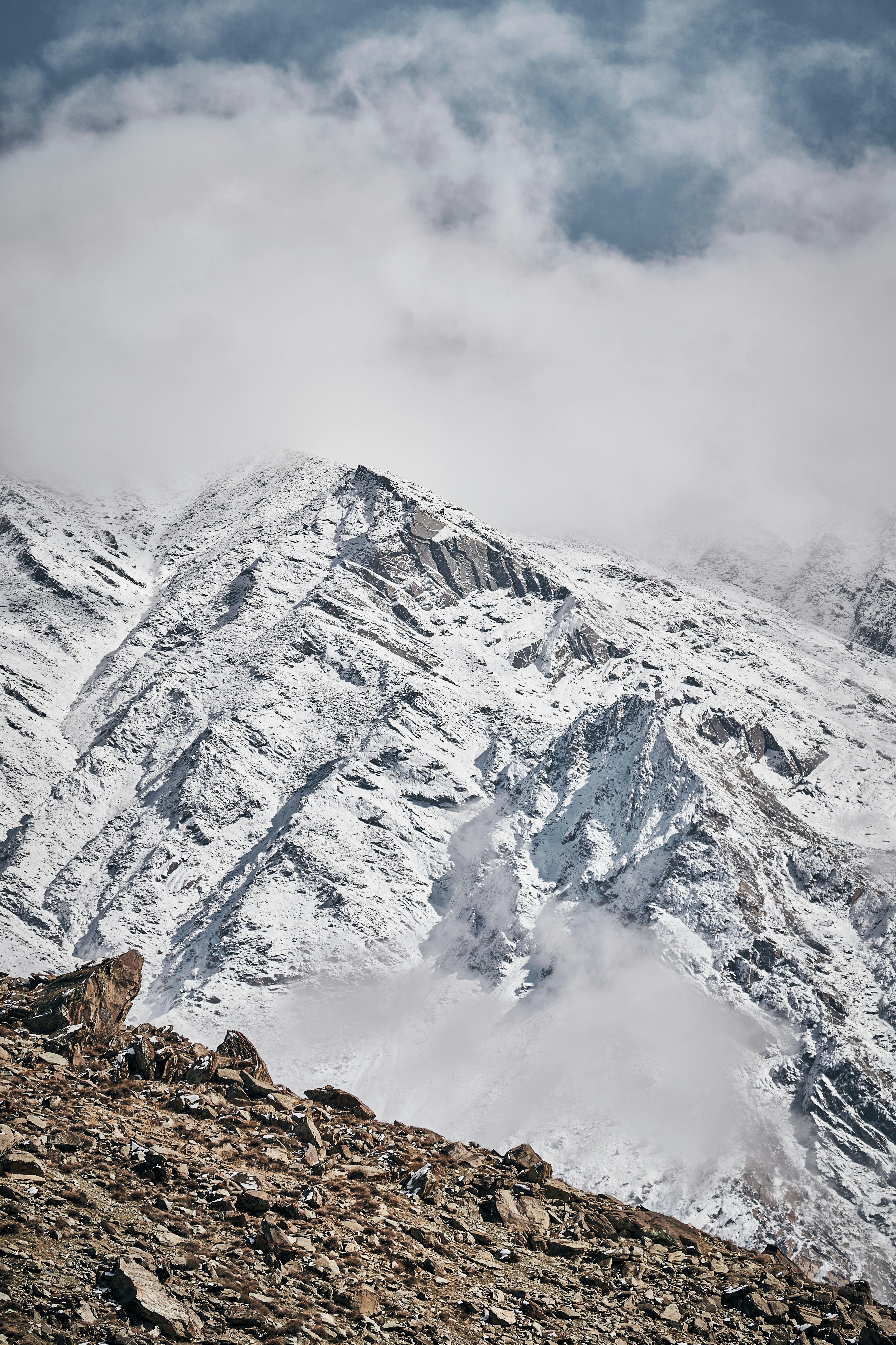 Snow-covered mountain peaks partially obscured by low clouds above a rocky foreground