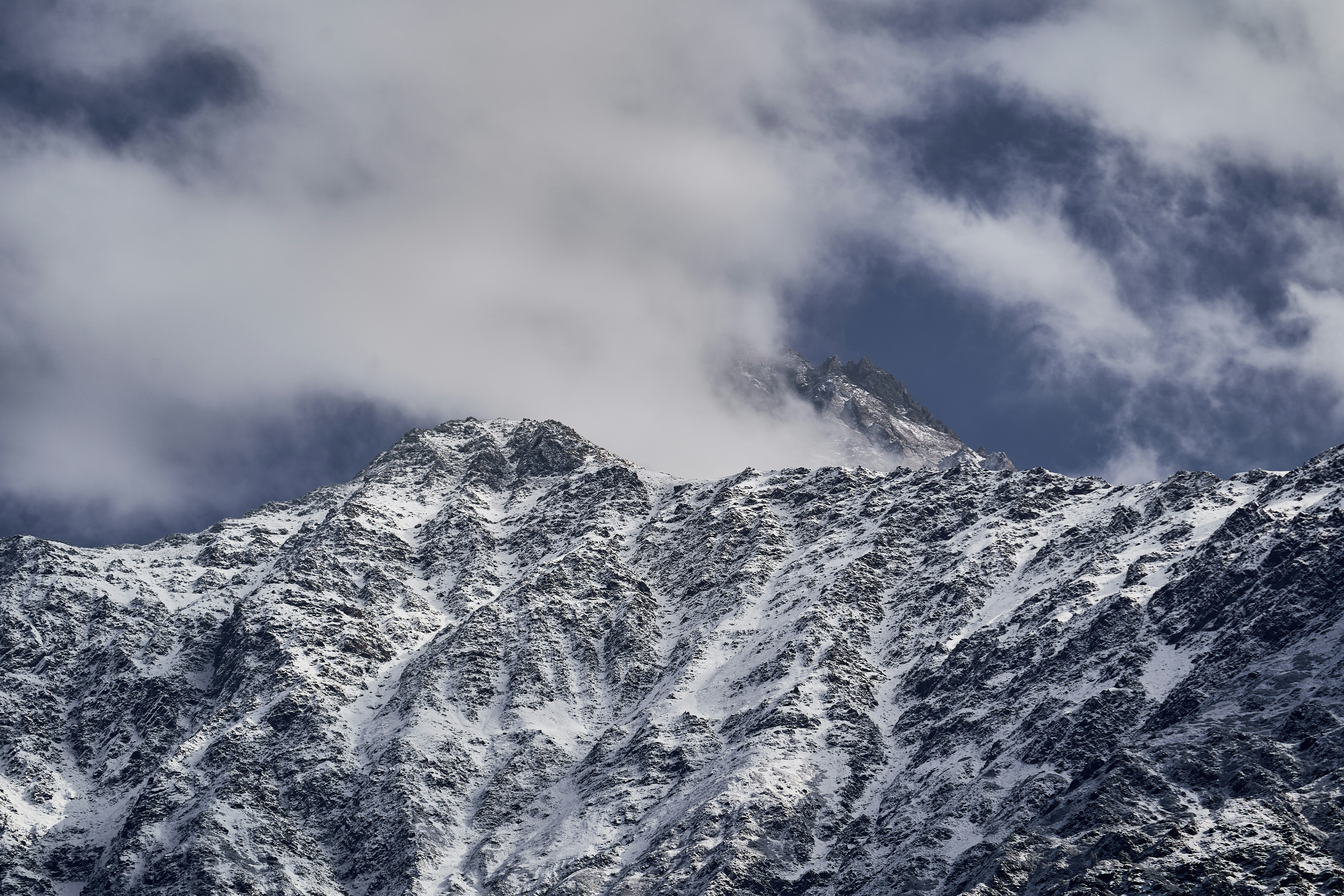 Snow covered mountain peaks partially obscured by thick white clouds against a blue sky