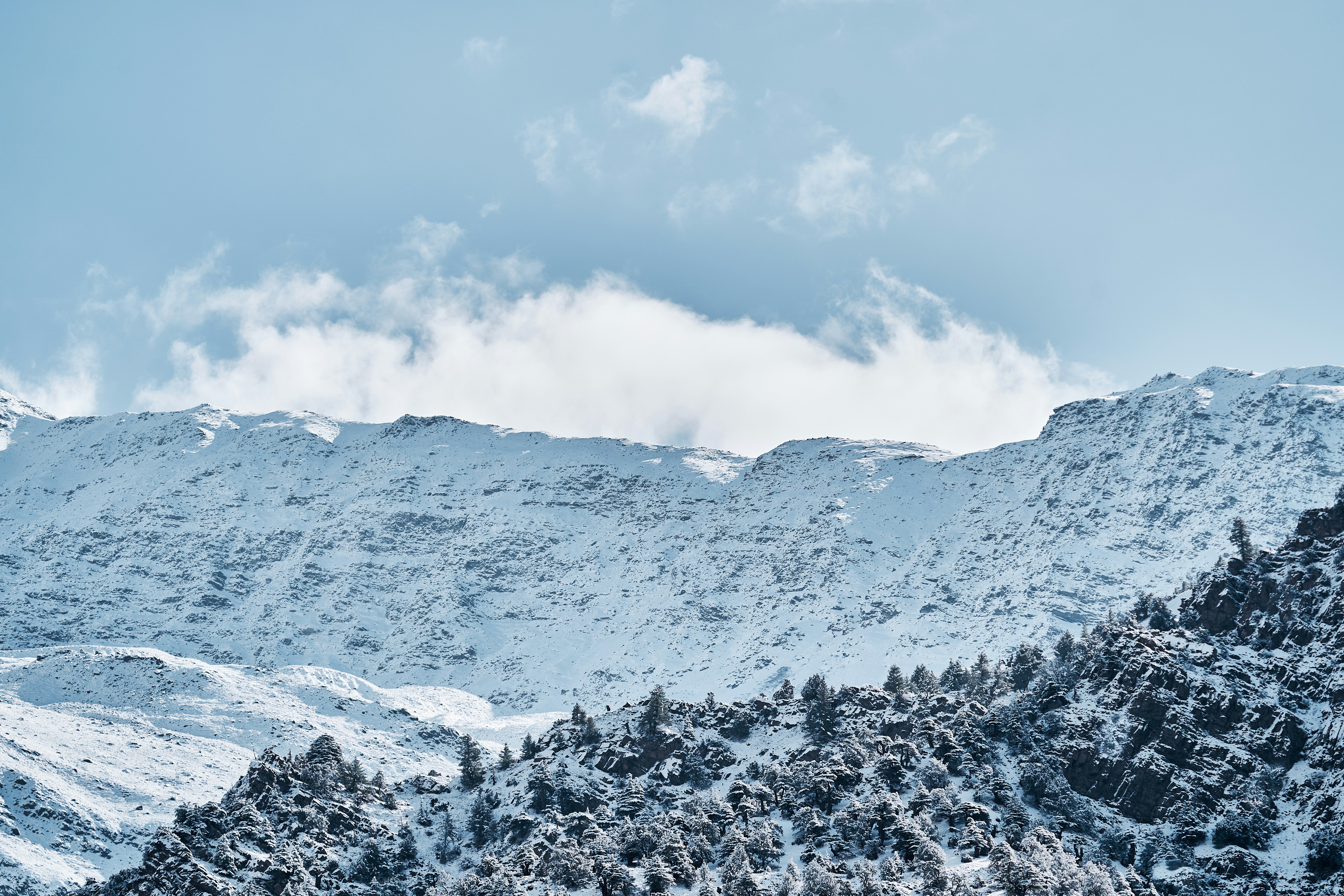 Snow covered mountain peaks under a bright blue sky with scattered white clouds