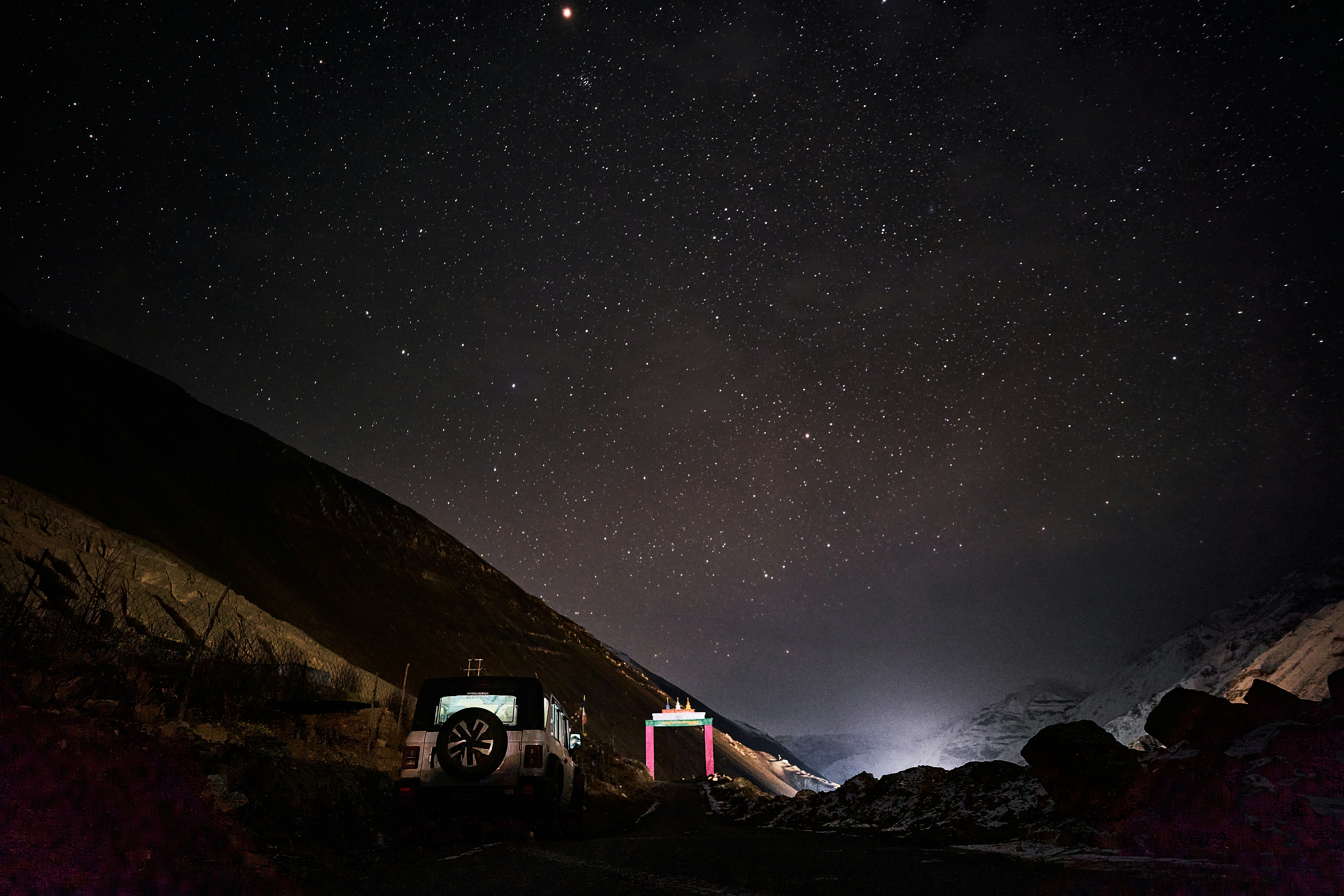 An off-road vehicle parked on a dark mountain road under a starry night sky