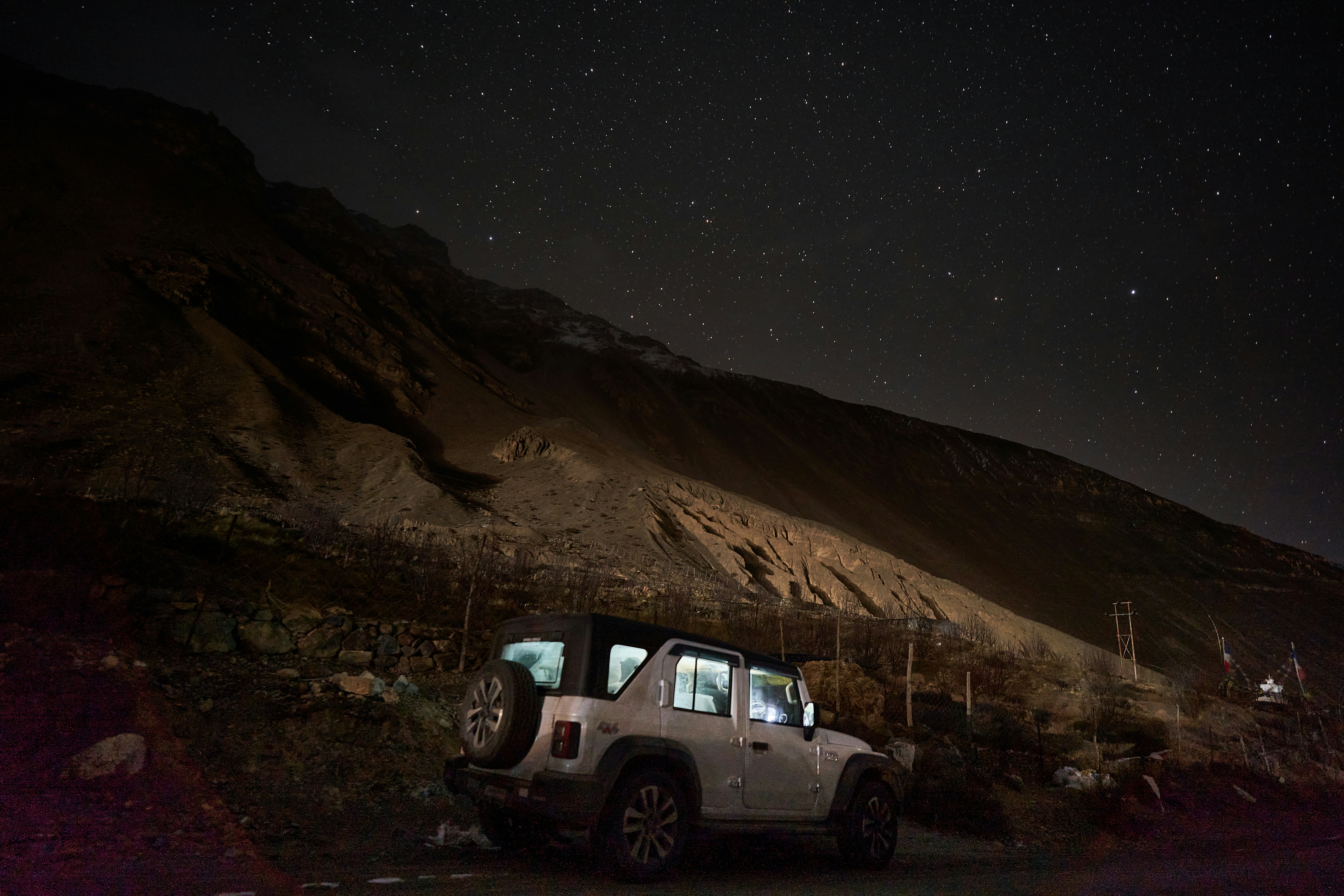 A white off-road vehicle parked beneath a starry night sky near a mountain