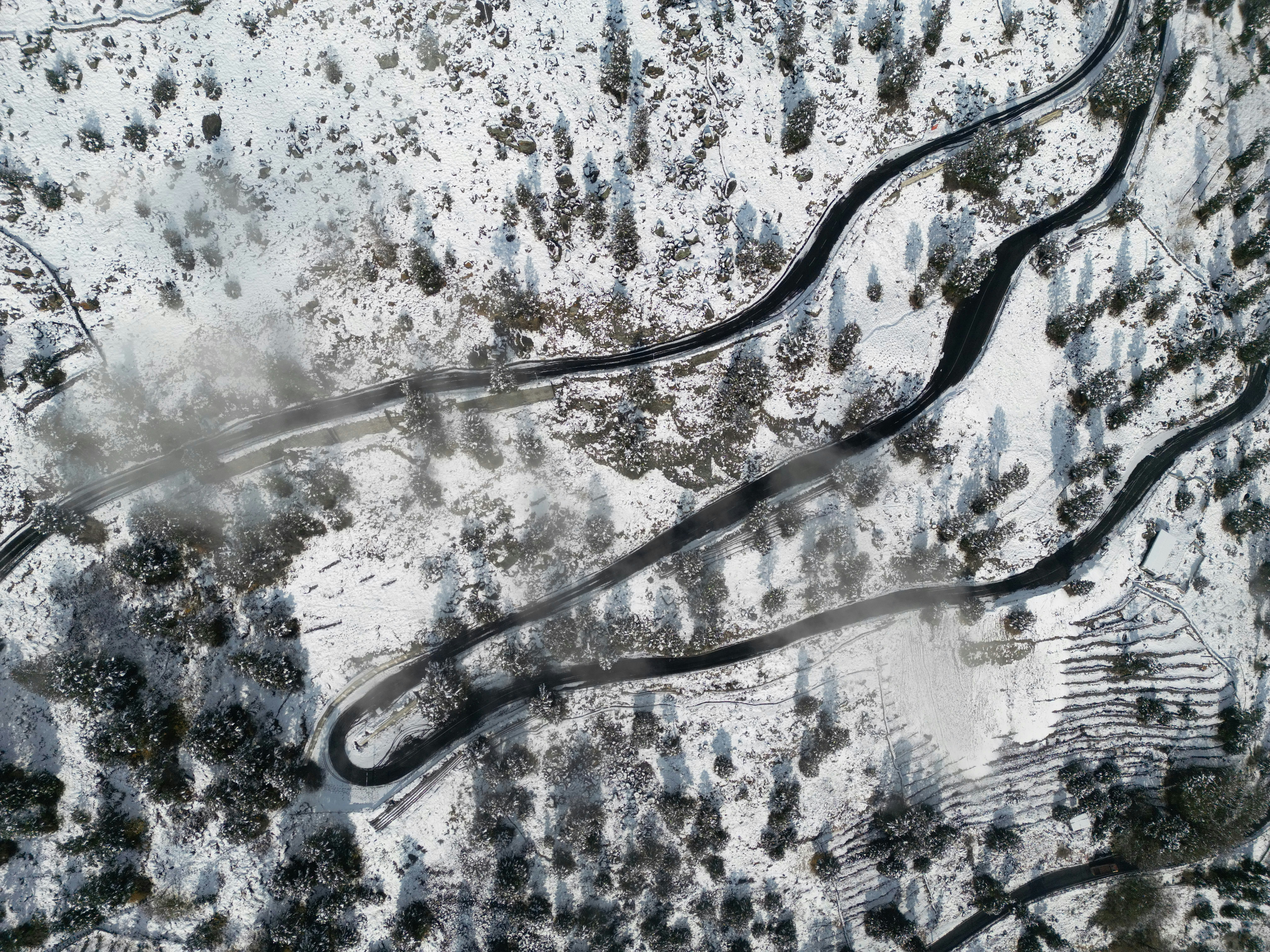 Aerial view of a winding road through a snowy forest with patches of fog