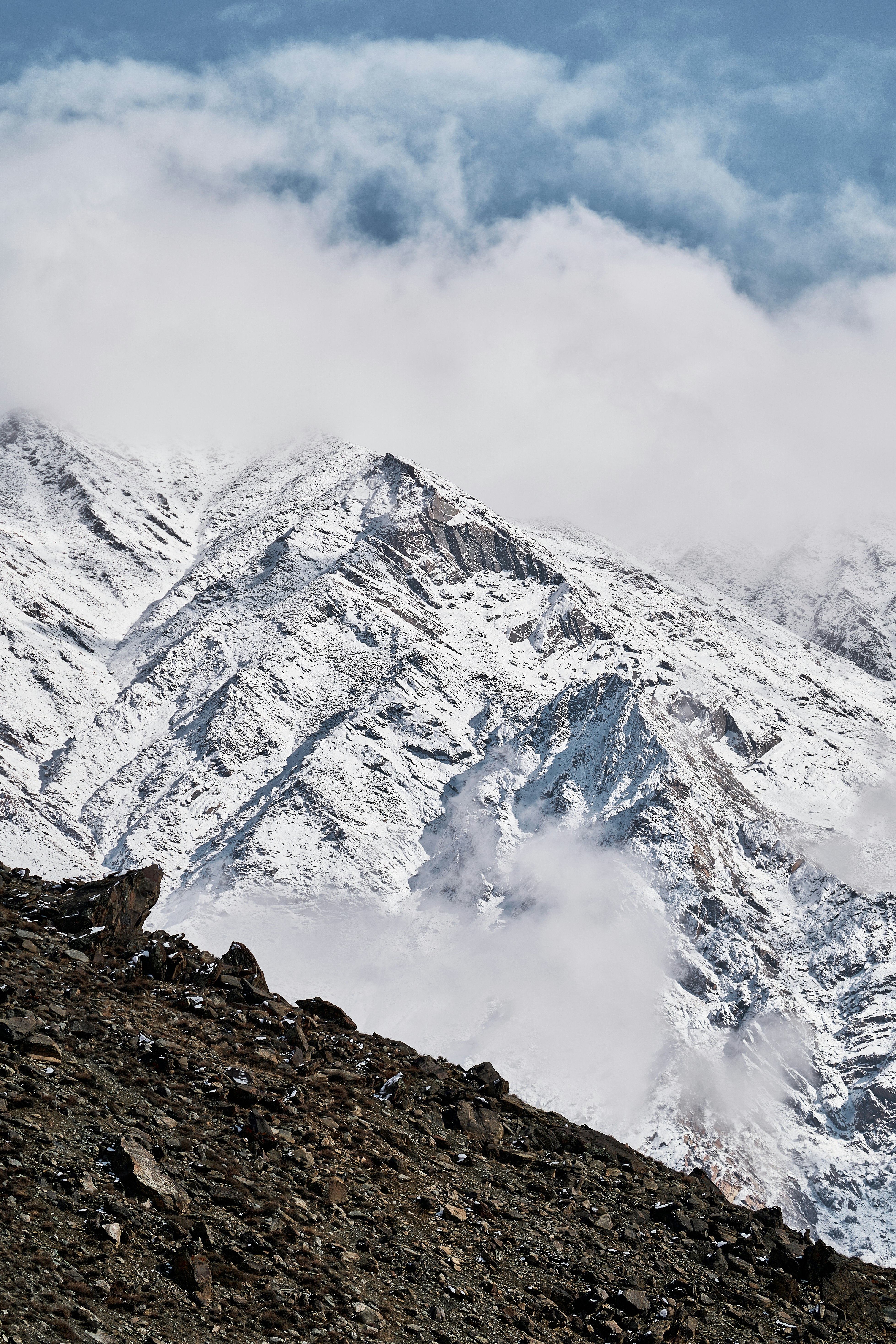Snow-covered mountain peaks rising above a rocky foreground with low clouds