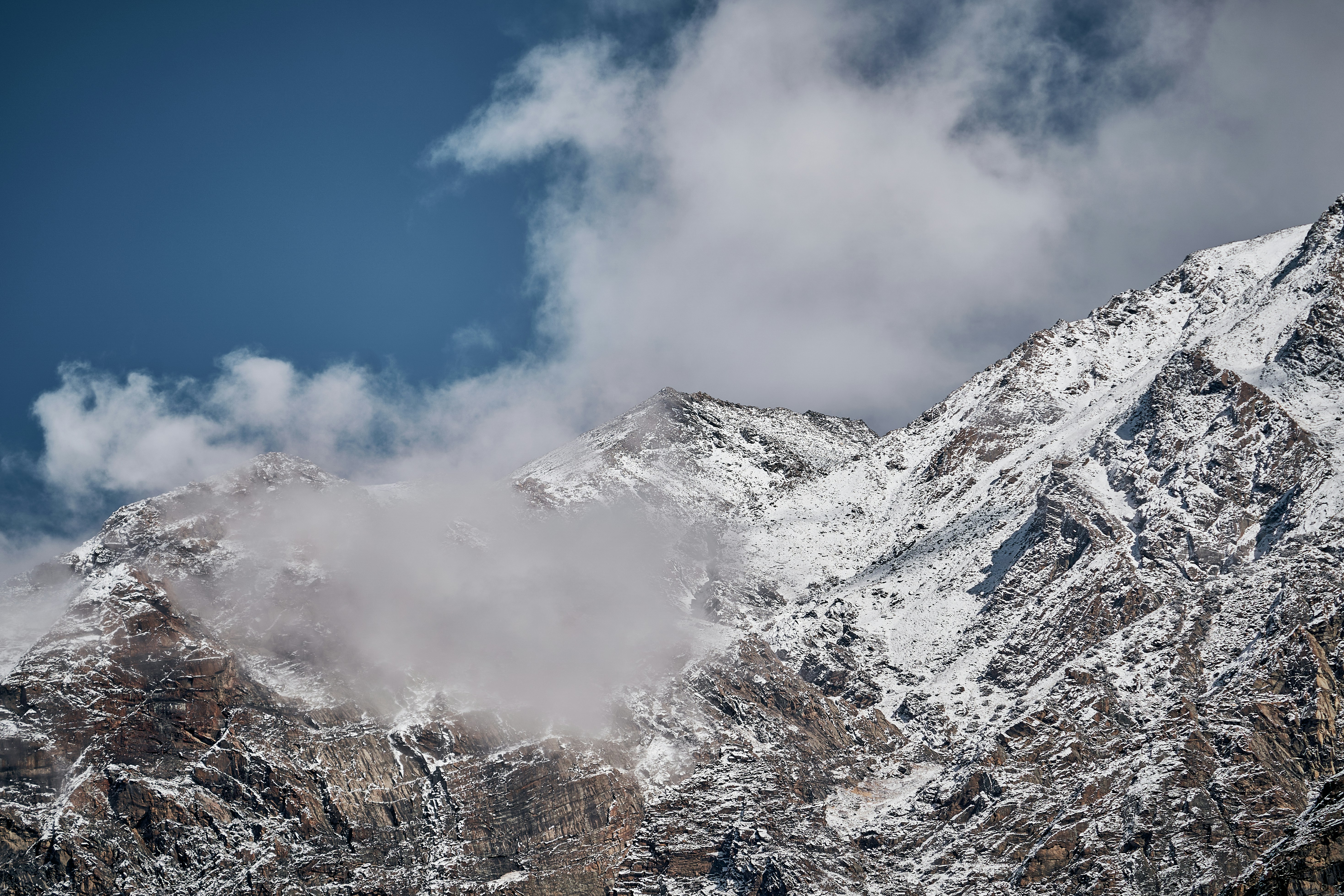 Snow covered mountain peaks under a blue sky with scattered white clouds