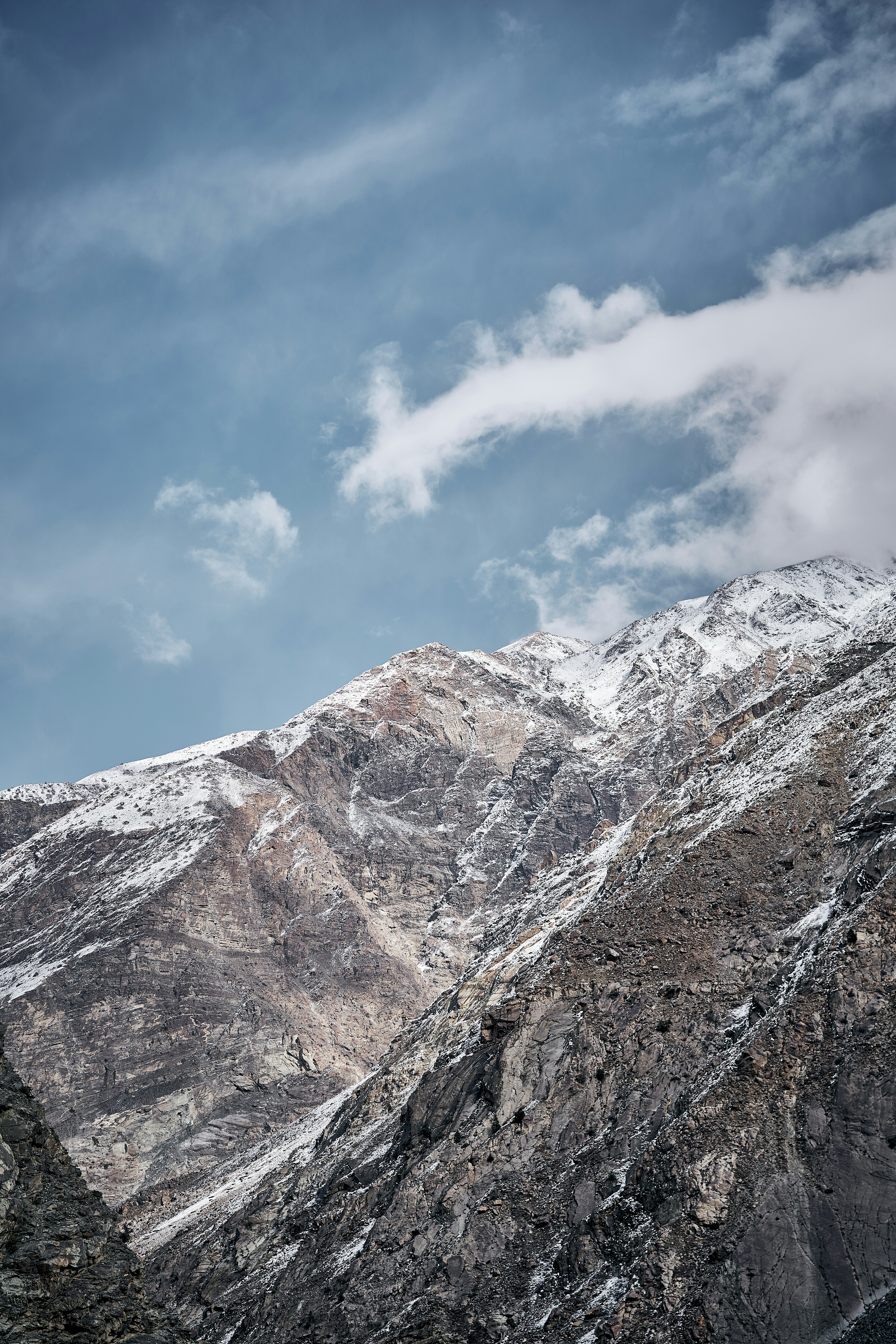 Snow-dusted rocky mountain peaks under a blue sky with scattered white clouds