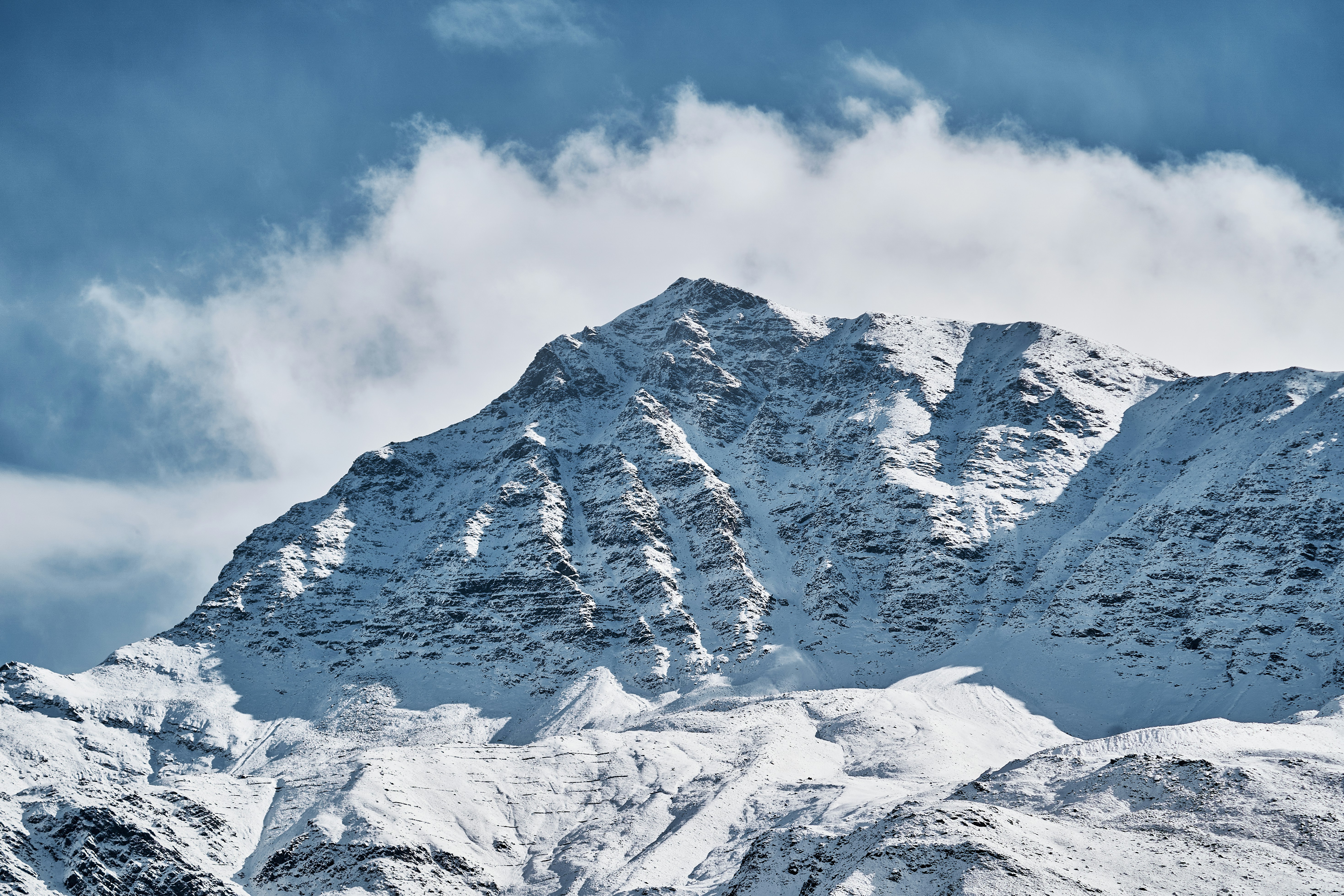 A snow covered mountain peak under a blue sky with scattered white clouds