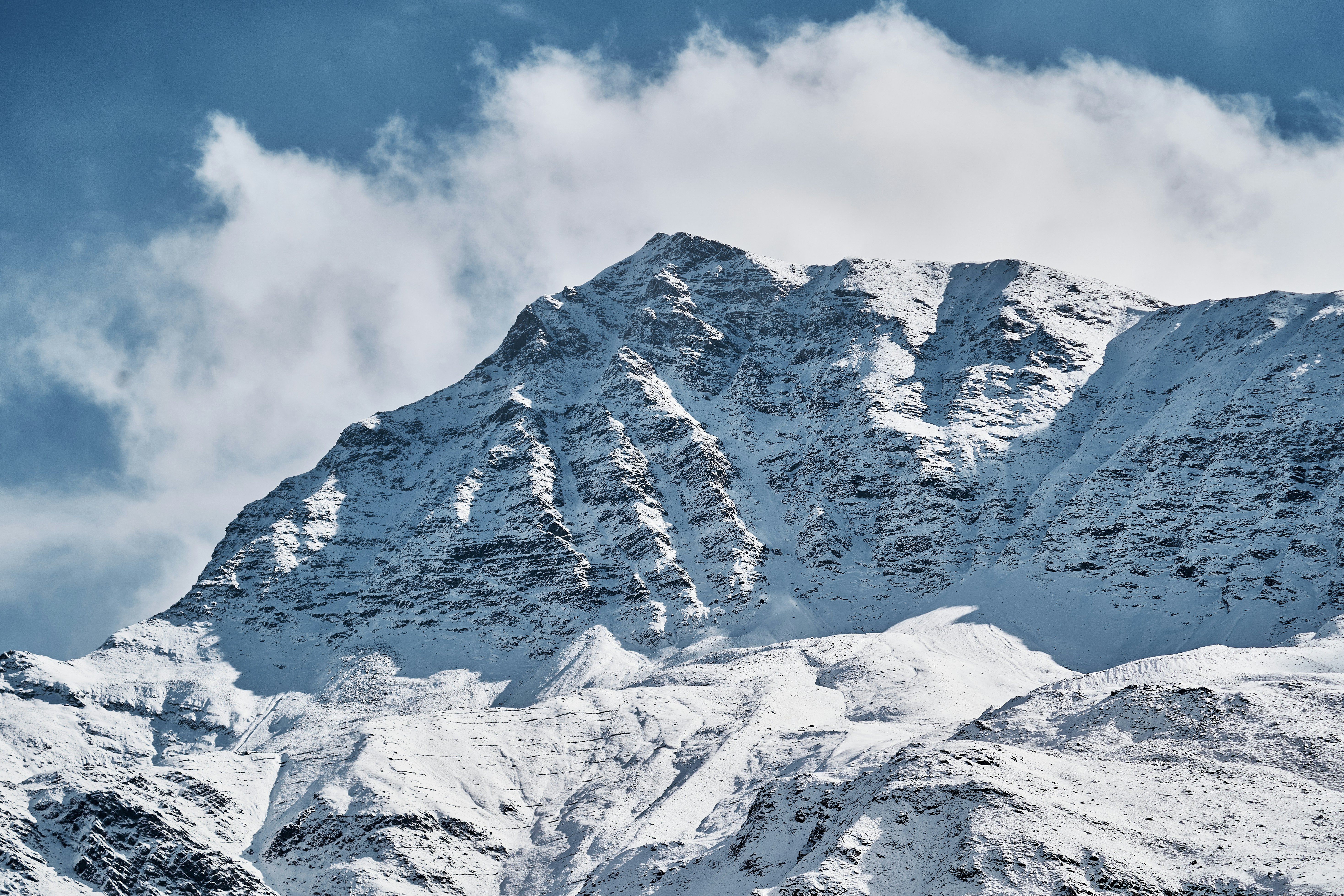 A snow covered mountain peak under a bright blue sky with white clouds