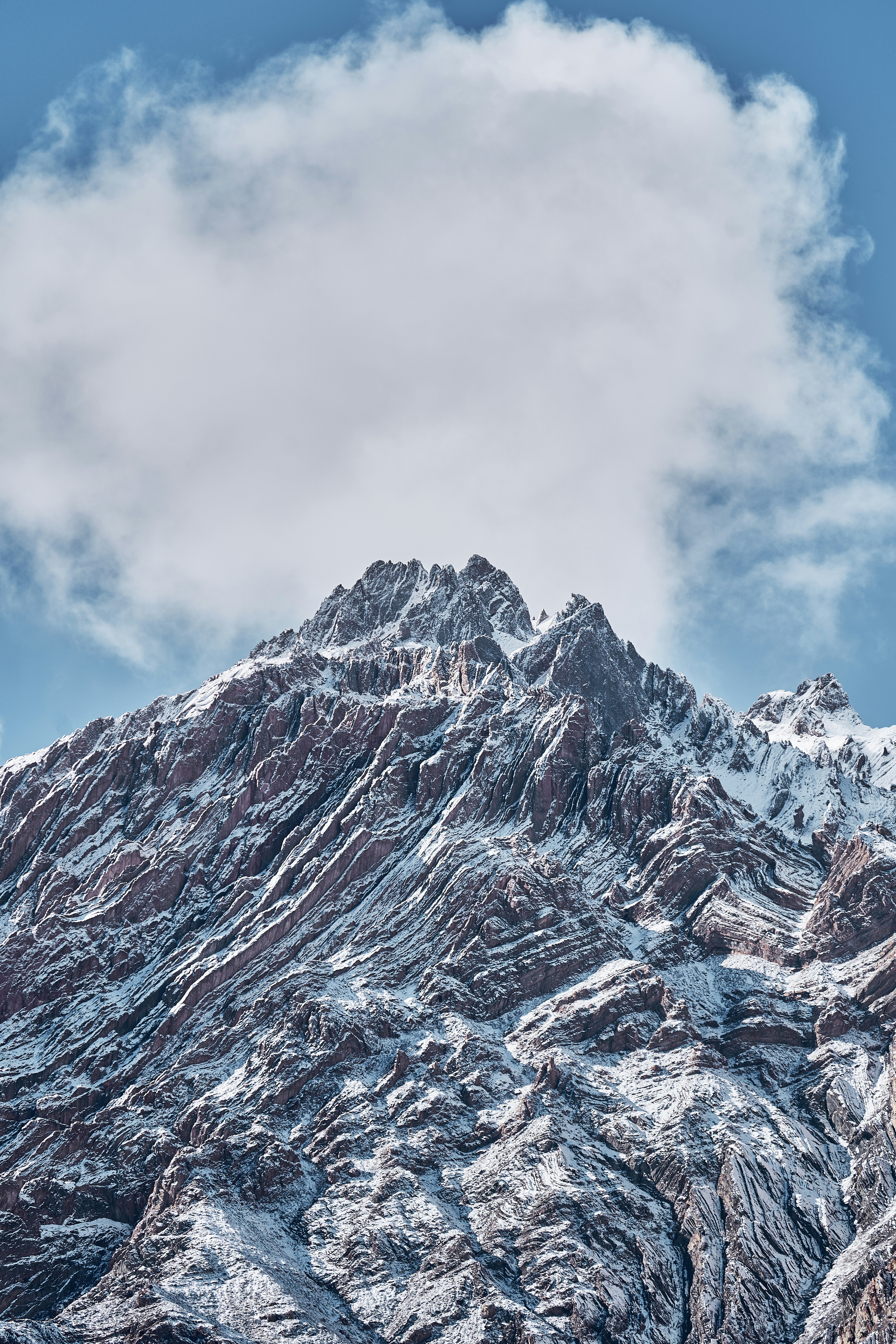 A jagged snow-covered mountain peak beneath a single large white cloud