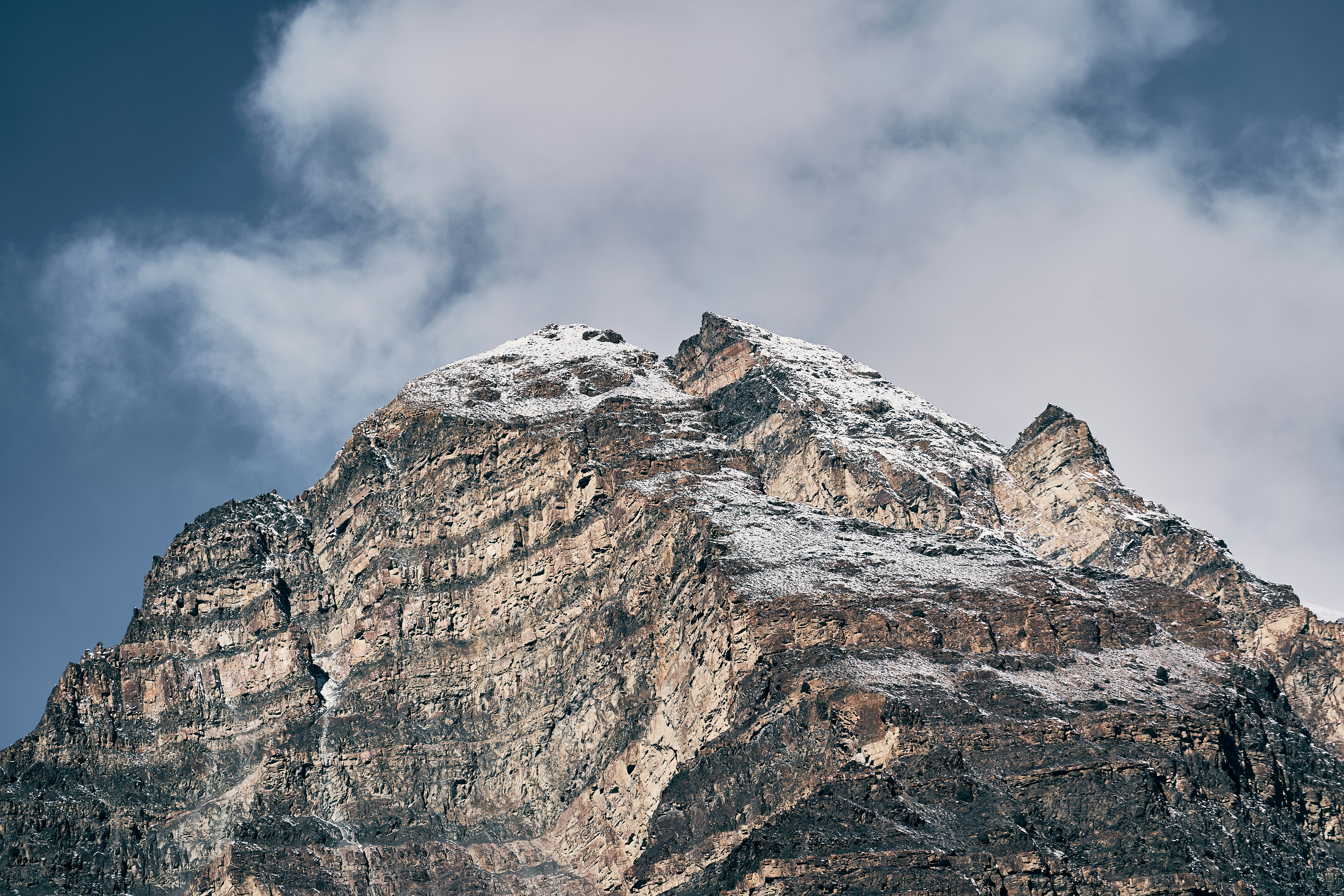 A jagged mountain peak with snow on the summit against a cloudy sky