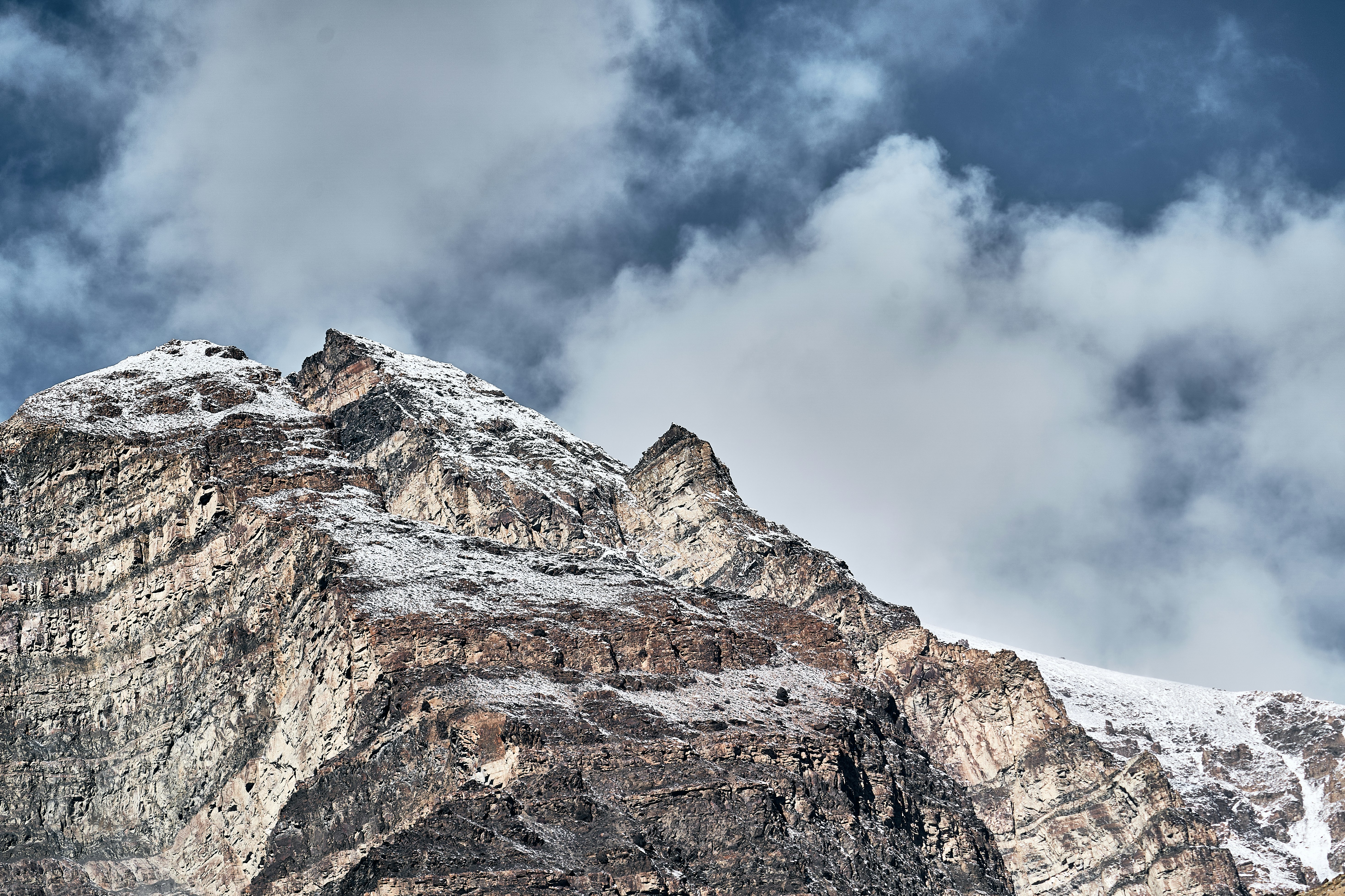 A jagged mountain peak with patches of snow under a cloudy sky